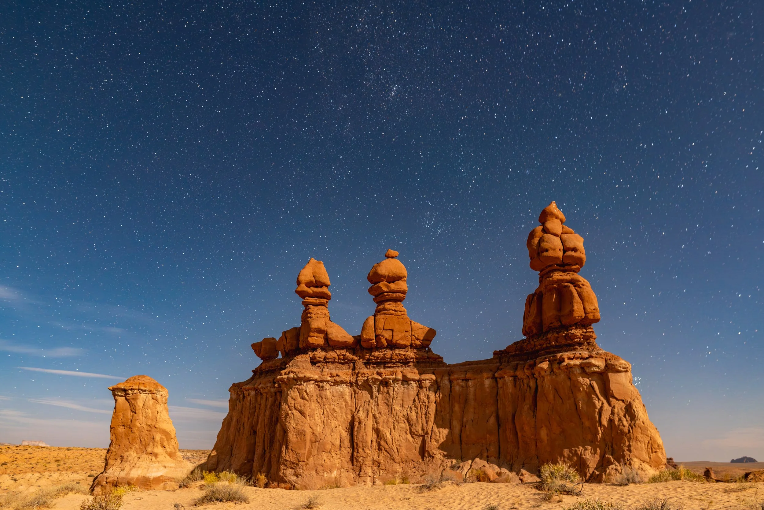 Goblin Valley
The famous "Three Sisters" rock formations of Goblin Valley State Park stand silhouetted against a brilliant Milky Way. These unique mushroom-shaped "hoodoos" are composed of Entrada Sandstone, eroded over millions of years. This shot c