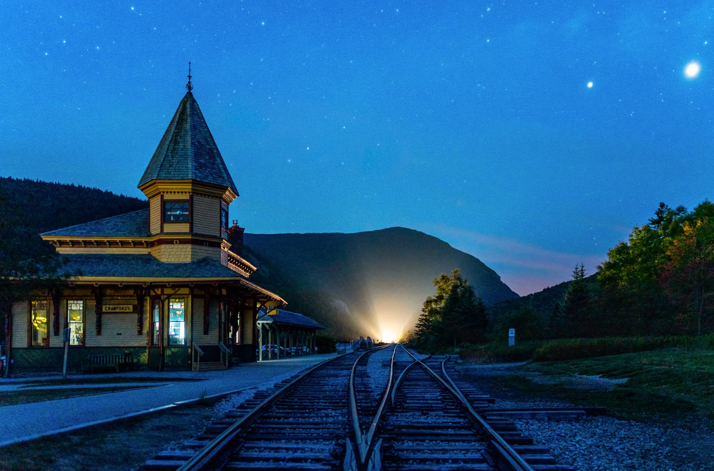 Nightfall at Crawford Notch
The historic Crawford Notch Depot stands as a warm, wooden sentinel against the cooling blue of a New Hampshire mountain twilight. Built in 1891, this Victorian-style station served the Maine Central Railroad and now acts 