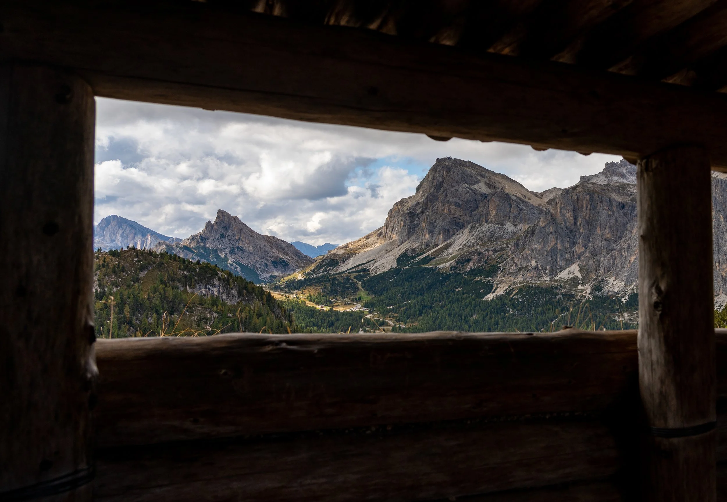 Alpine Window
A unique perspective of the Dolomites framed through the dark timber window of a World War I bunker. The natural wooden frame provides a sense of warmth and shelter, contrasting with the expansive, jagged limestone peaks and rolling gre