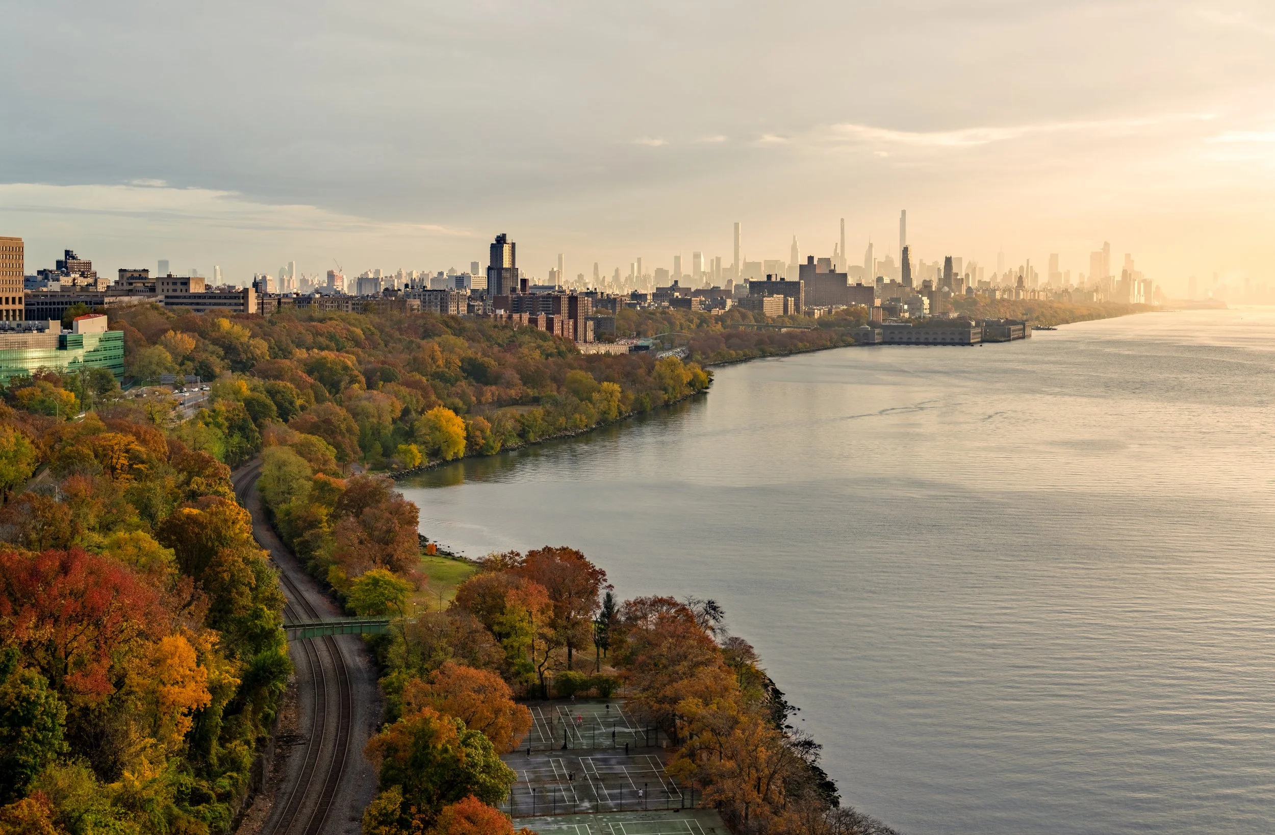 A Different Perspective
A sweeping, high-altitude view looking north along the Hudson River from the George Washington Bridge. This shot captures the lush greenery of the Fort Tryon Park area and the Henry Hudson Parkway as they snake alongside the w