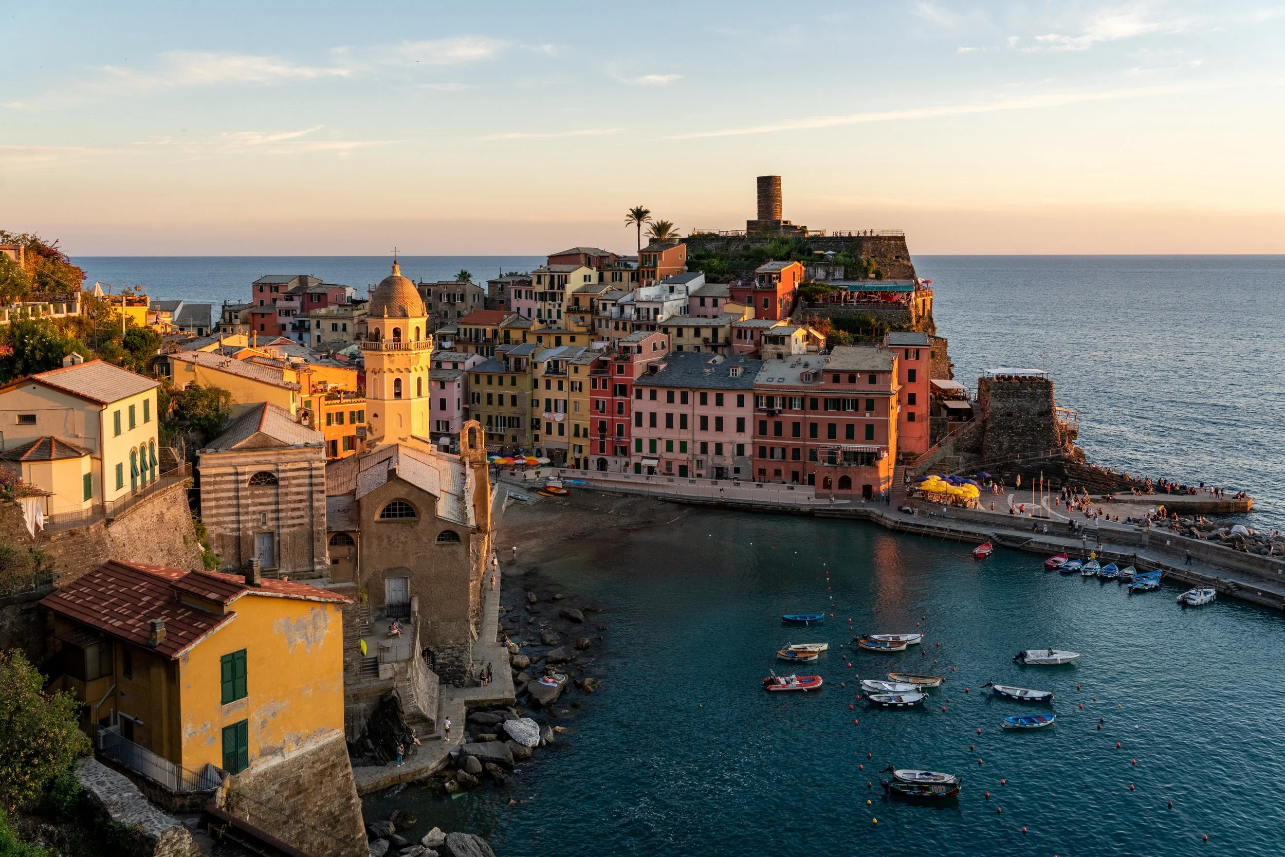 The Jewel of the Riviera
A classic, high-angle view of Vernazza along the Cinque Terre coast. The vibrant, multi-colored buildings contrast sharply with the deep azure of the Mediterranean, while the rugged cliffs and terraced hillsides emphasize the