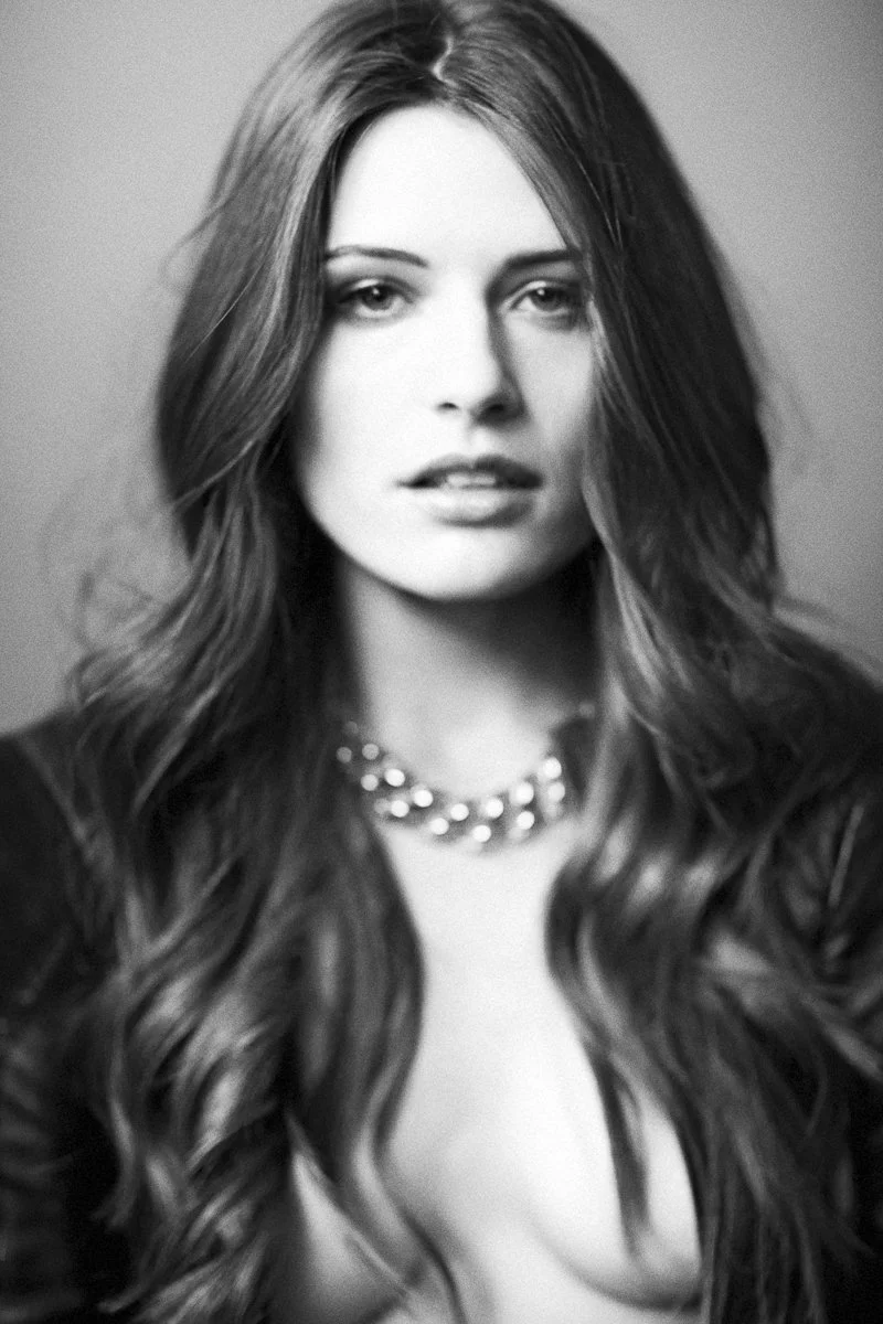 Black and white portrait of a woman with long wavy hair, wearing a pearl necklace and a dark top.