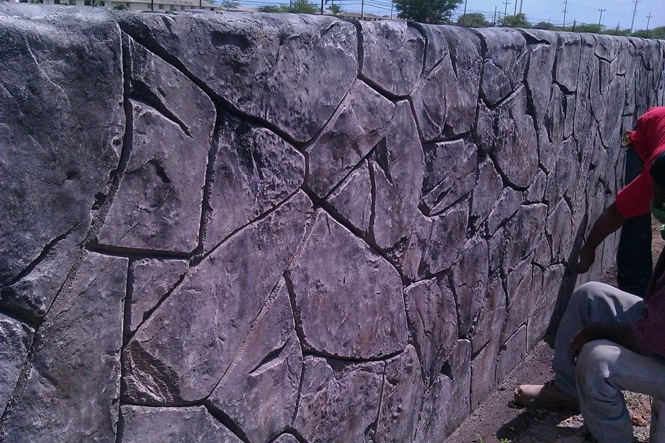 A stone wall made of irregularly shaped stones, with a few people sitting or standing nearby.