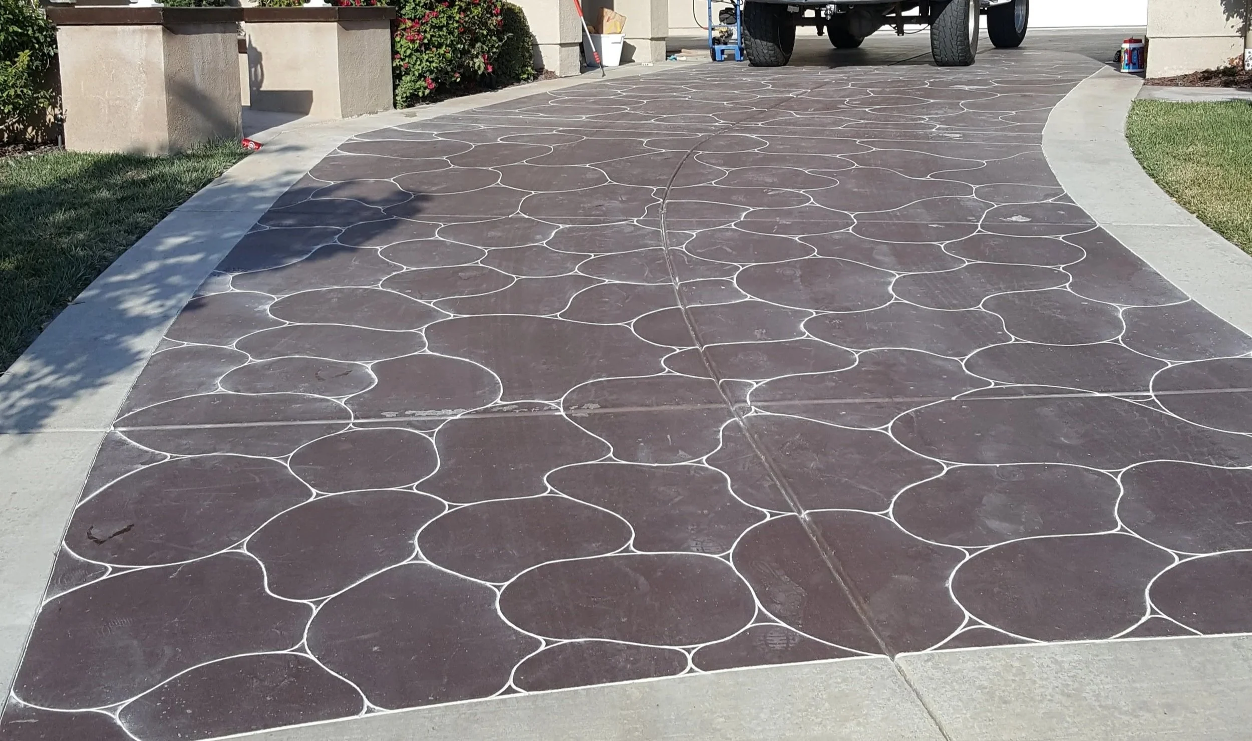 Close-up of a concrete driveway with decorative circular patterns outlined in white, leading to a garage area with a vehicle and gardening tools.