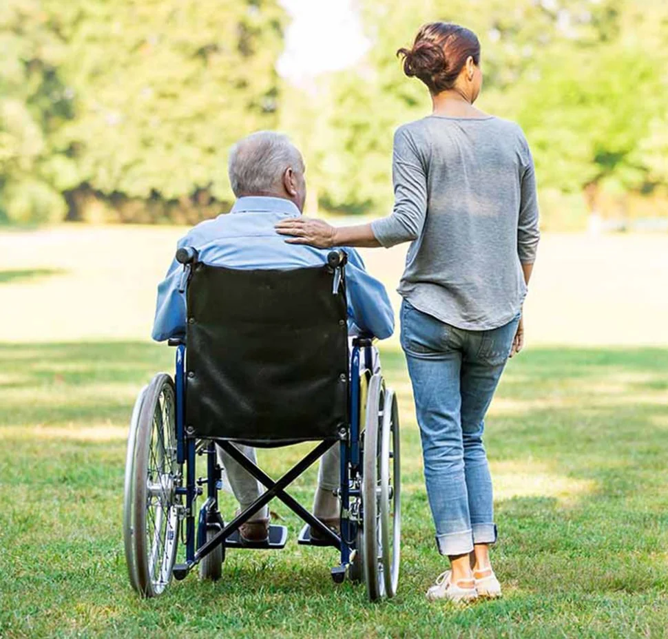 A woman walks beside a man in a wheelchair in a park.