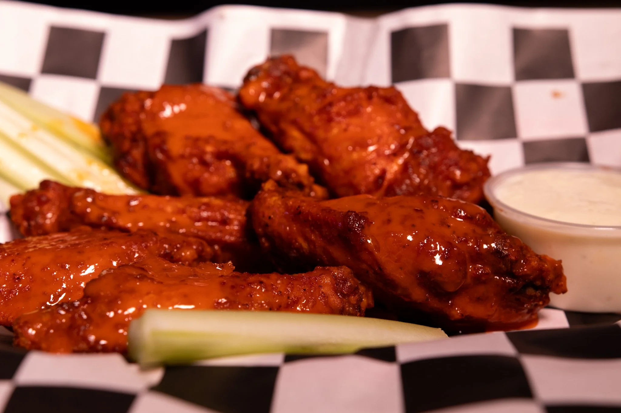 Buffalo chicken wings with celery sticks and a side of ranch dressing on black and white checkered paper