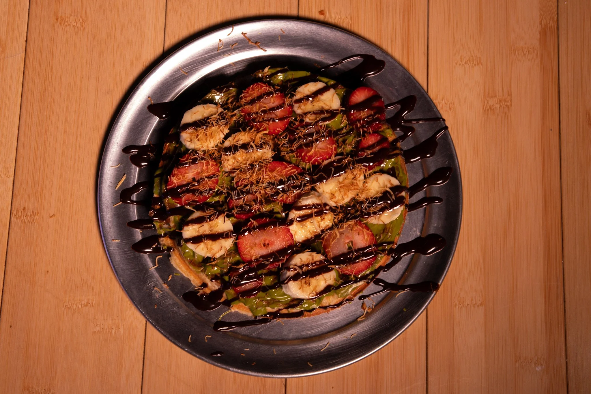 Fruit pizza topped with chocolate drizzle and shredded coconut on a metal platter