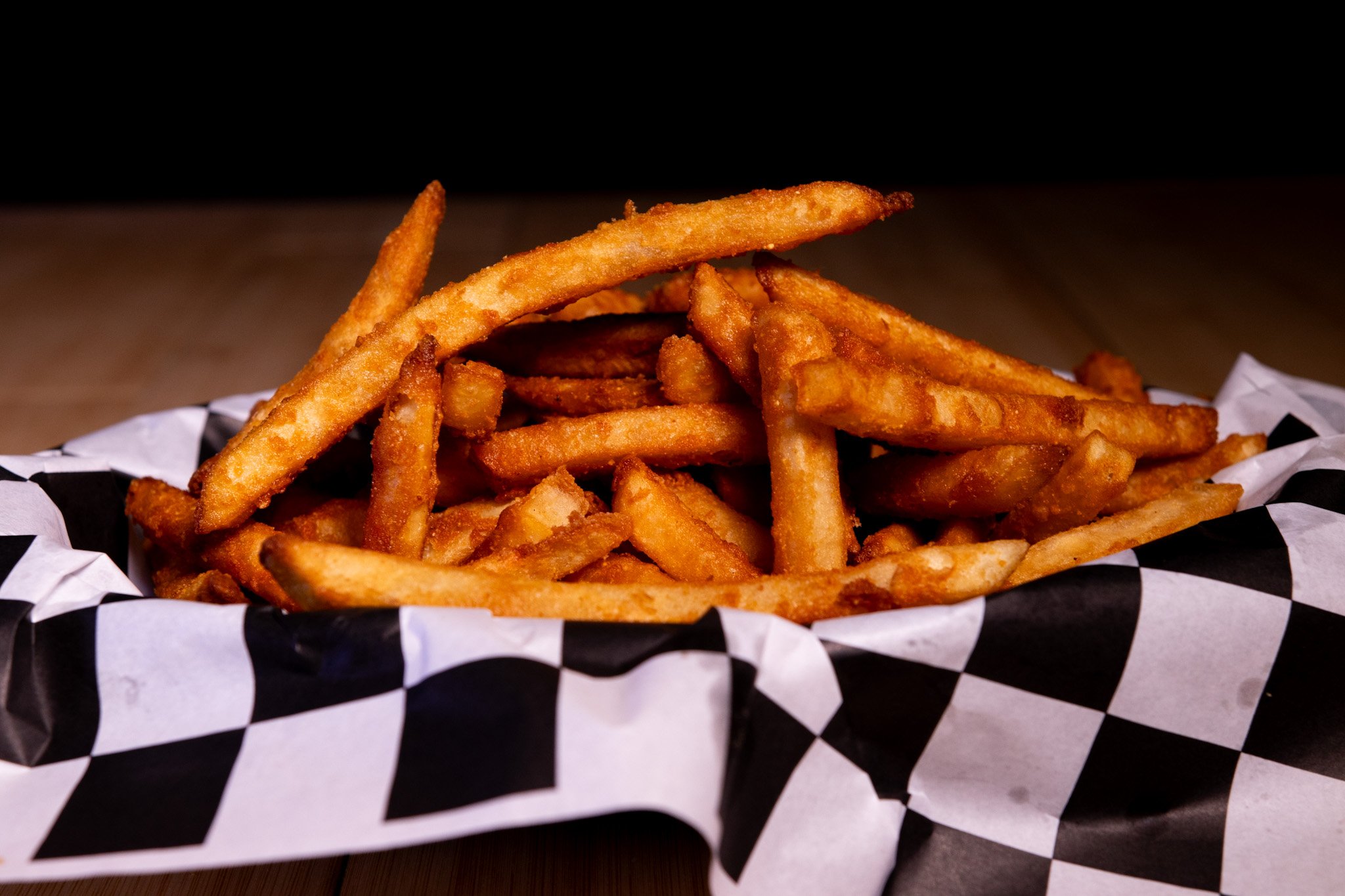 Pile of crispy French fries on black and white checkered paper