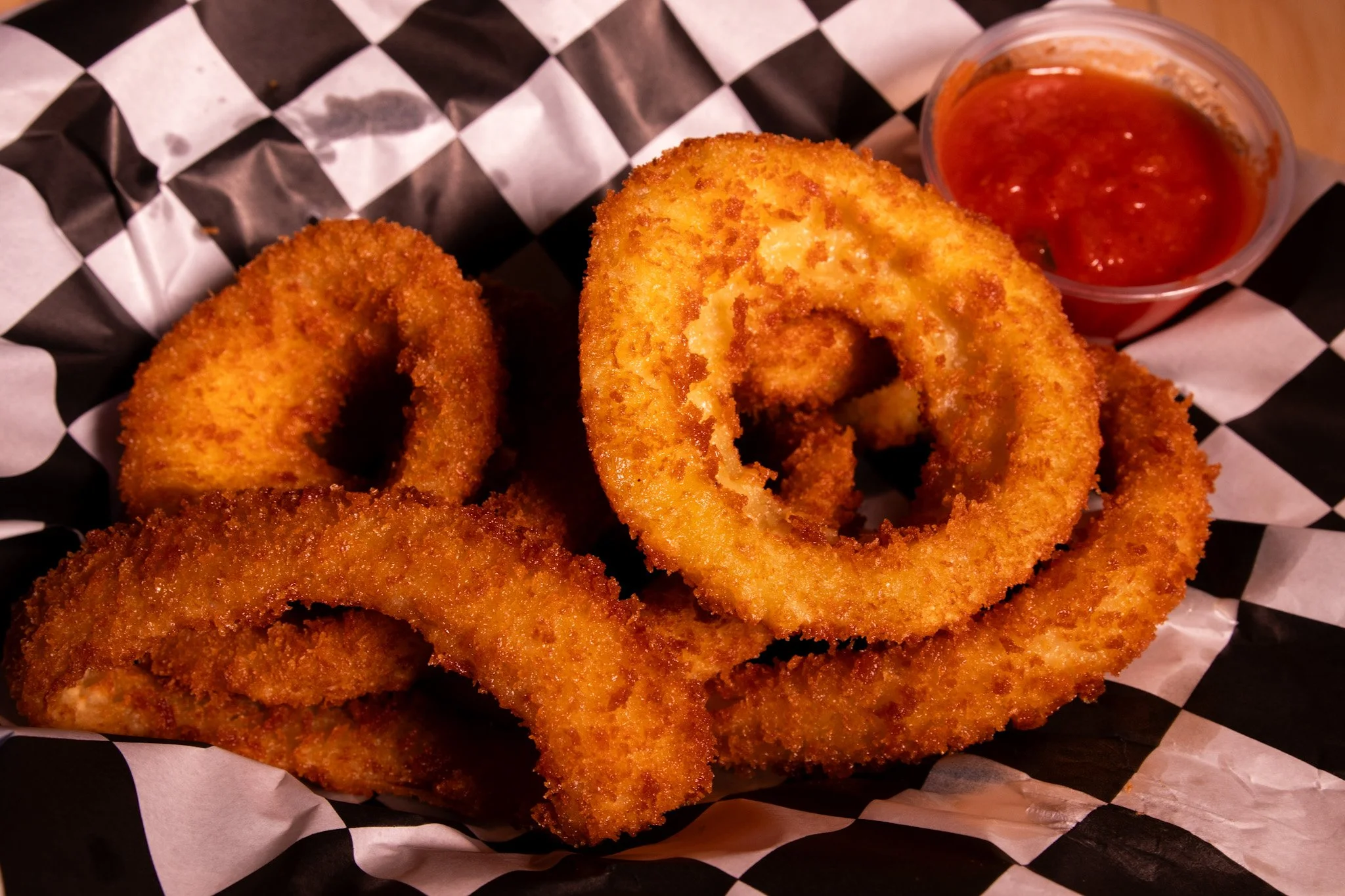 Fried onion rings with a side of marinara sauce on checkered paper