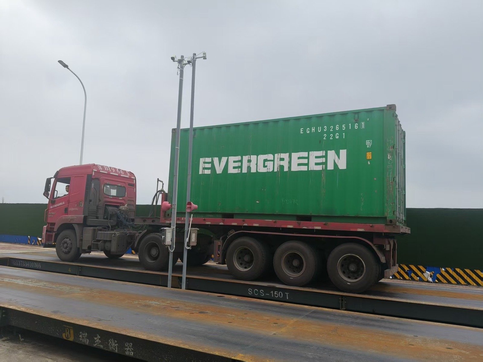 Red semi-truck with green shipping container labeled 'EVERGREEN' on a transportation flatbed.