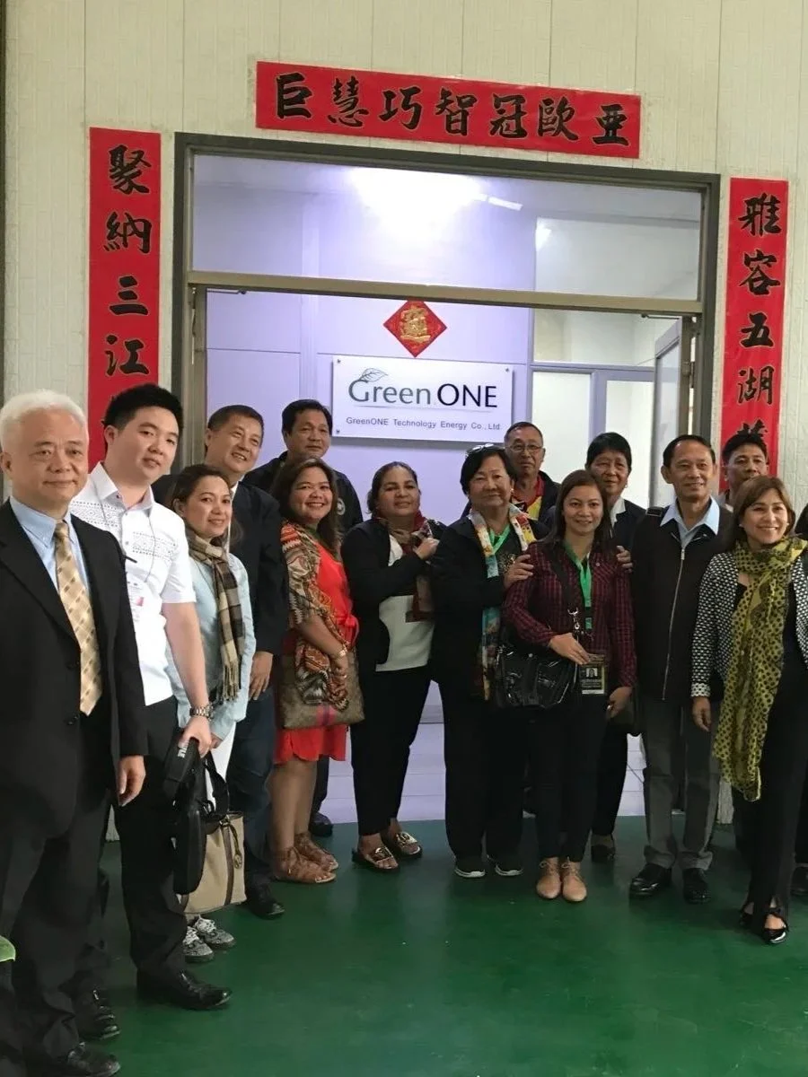 Group of people standing in front of a sign that says GreenONE, inside a building with a doorway decorated with red Chinese New Year banners.
