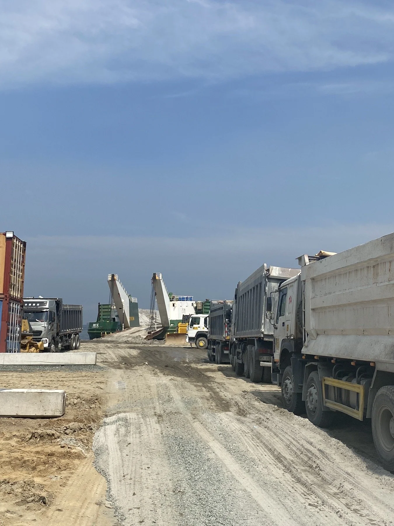 Construction site with trucks and a ferris wheel in the distance under a blue sky.