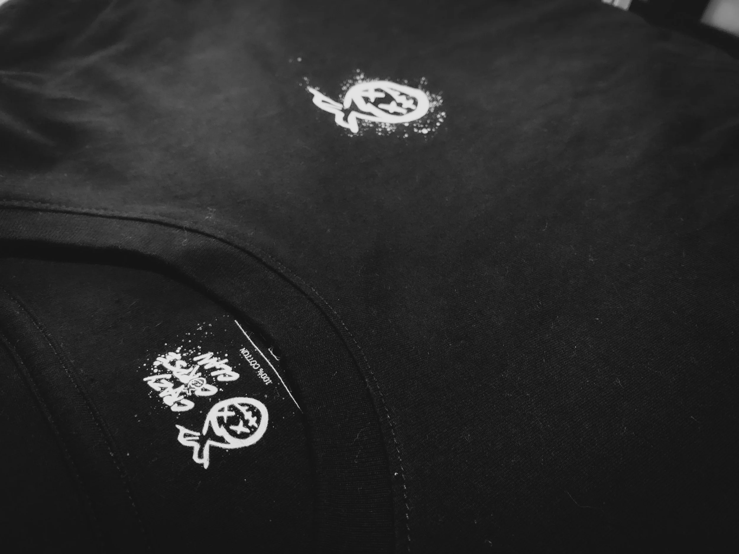 Close-up of a black hoodie with white printed logo and text on the inside collar area, showing part of the sleeve and the logo on the chest.