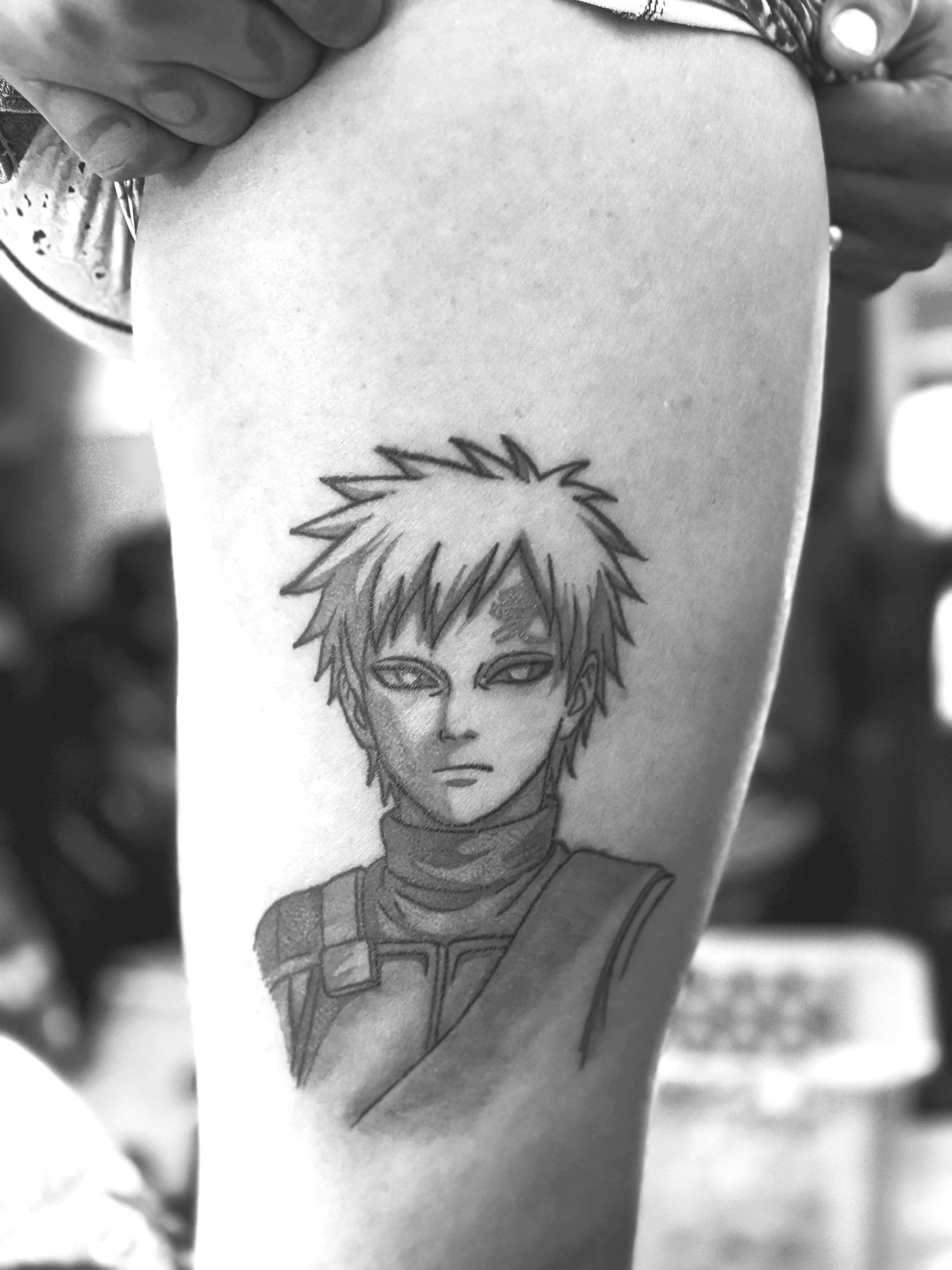 Black and white tattoo of anime character with spiky hair, intense eyes, and a serious expression, on a person's upper arm.