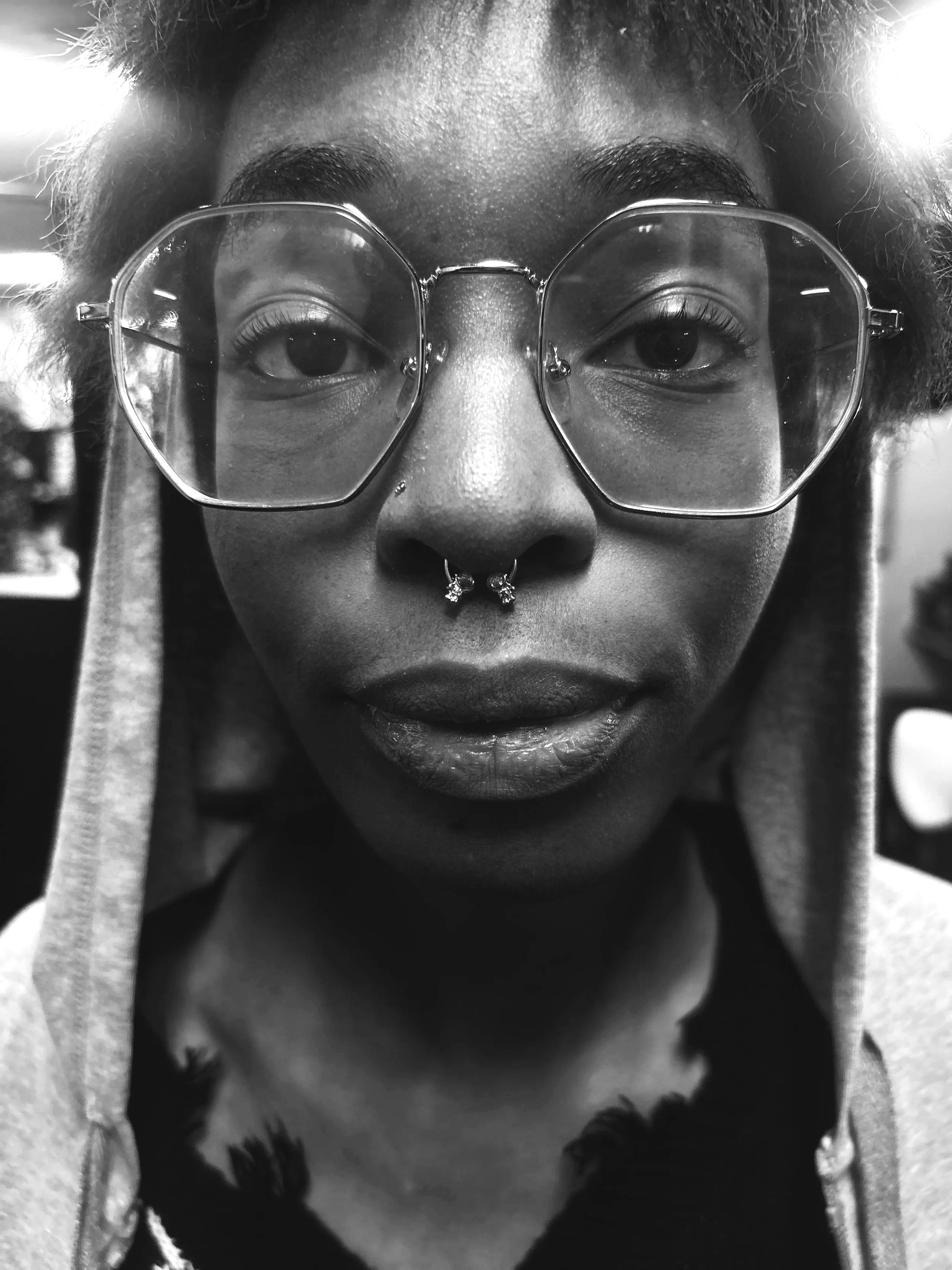 Close-up black and white photo of a woman with glasses, a septum piercing, and short hair, wearing a hoodie.