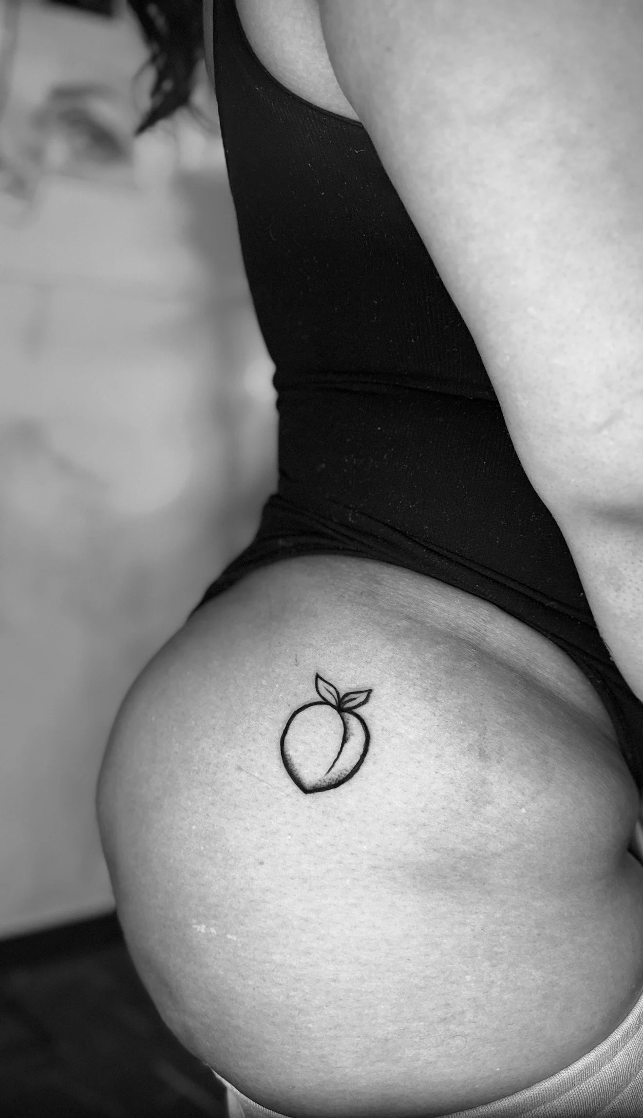 Black-and-white photo of a person's hip and thigh, showing a tattoo of a peach with leaves.