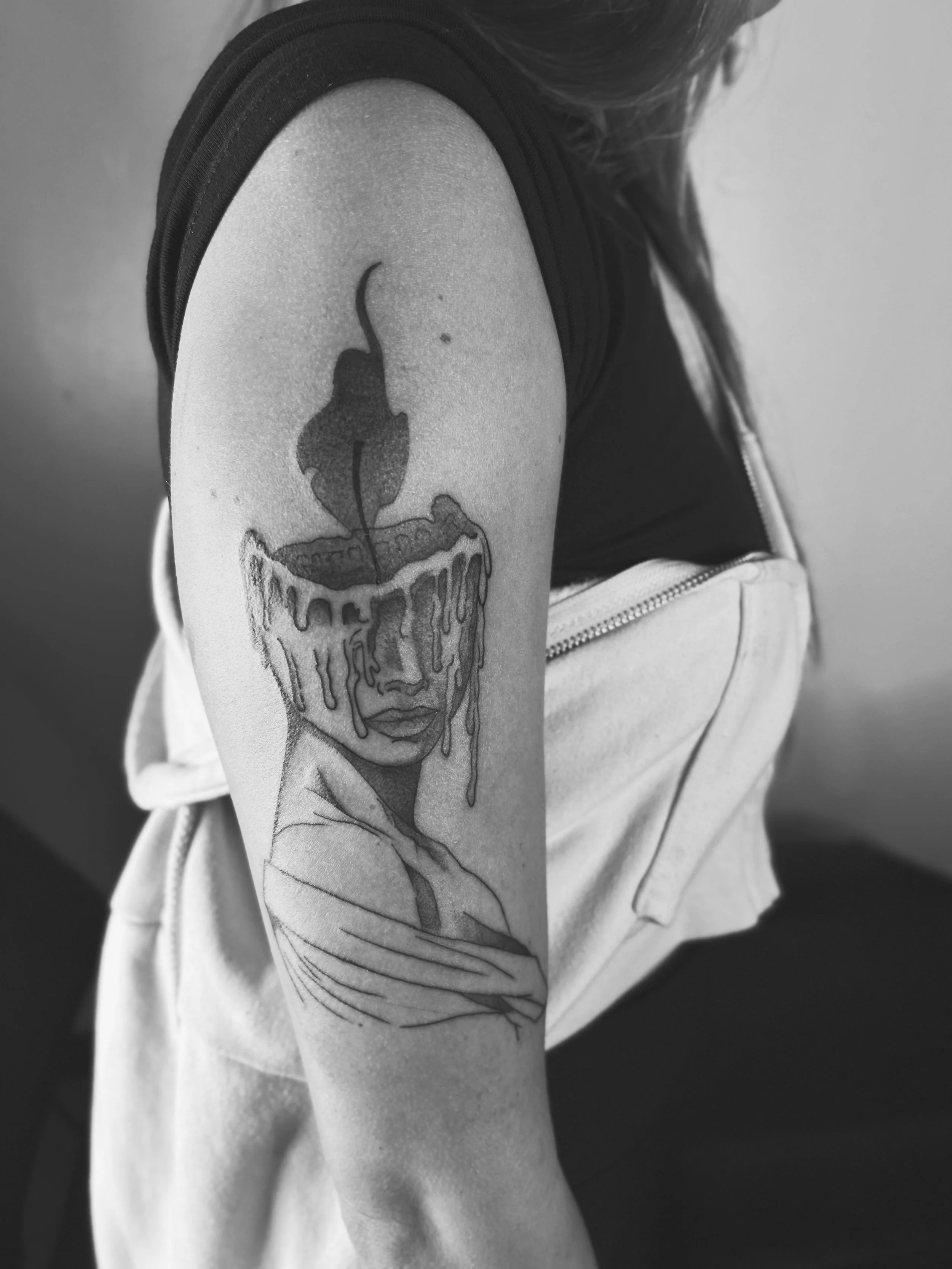Black and gray illustration tattoo of a woman with a cup on her head, melting, with a cherry on top, on a person's upper arm.
