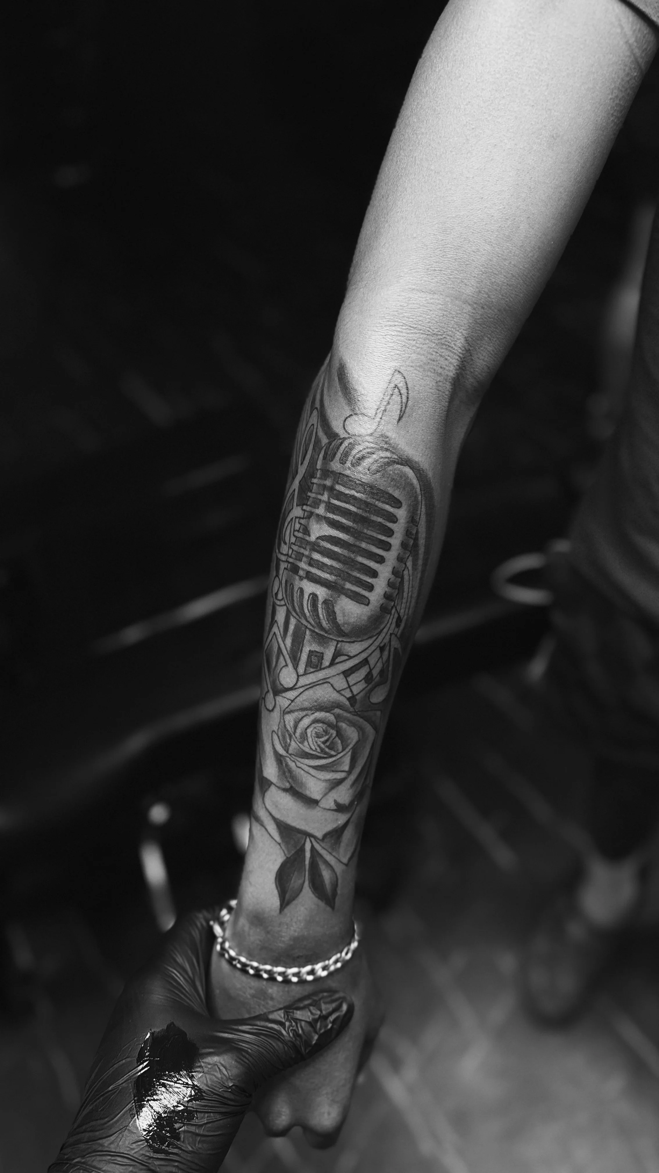 Tattoo of a vintage microphone and a rose on a person's forearm.