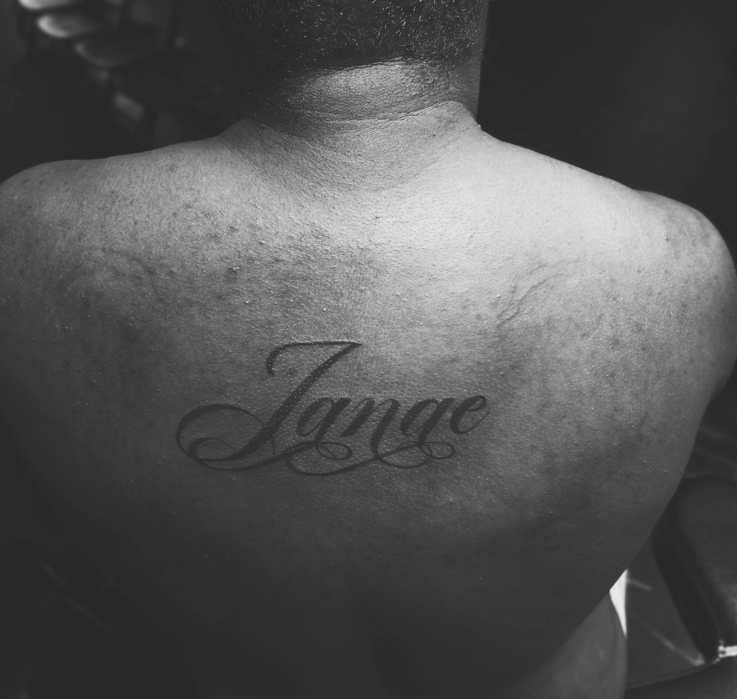 Back tattoo of the word 'Joyce' in cursive on a person's upper back.