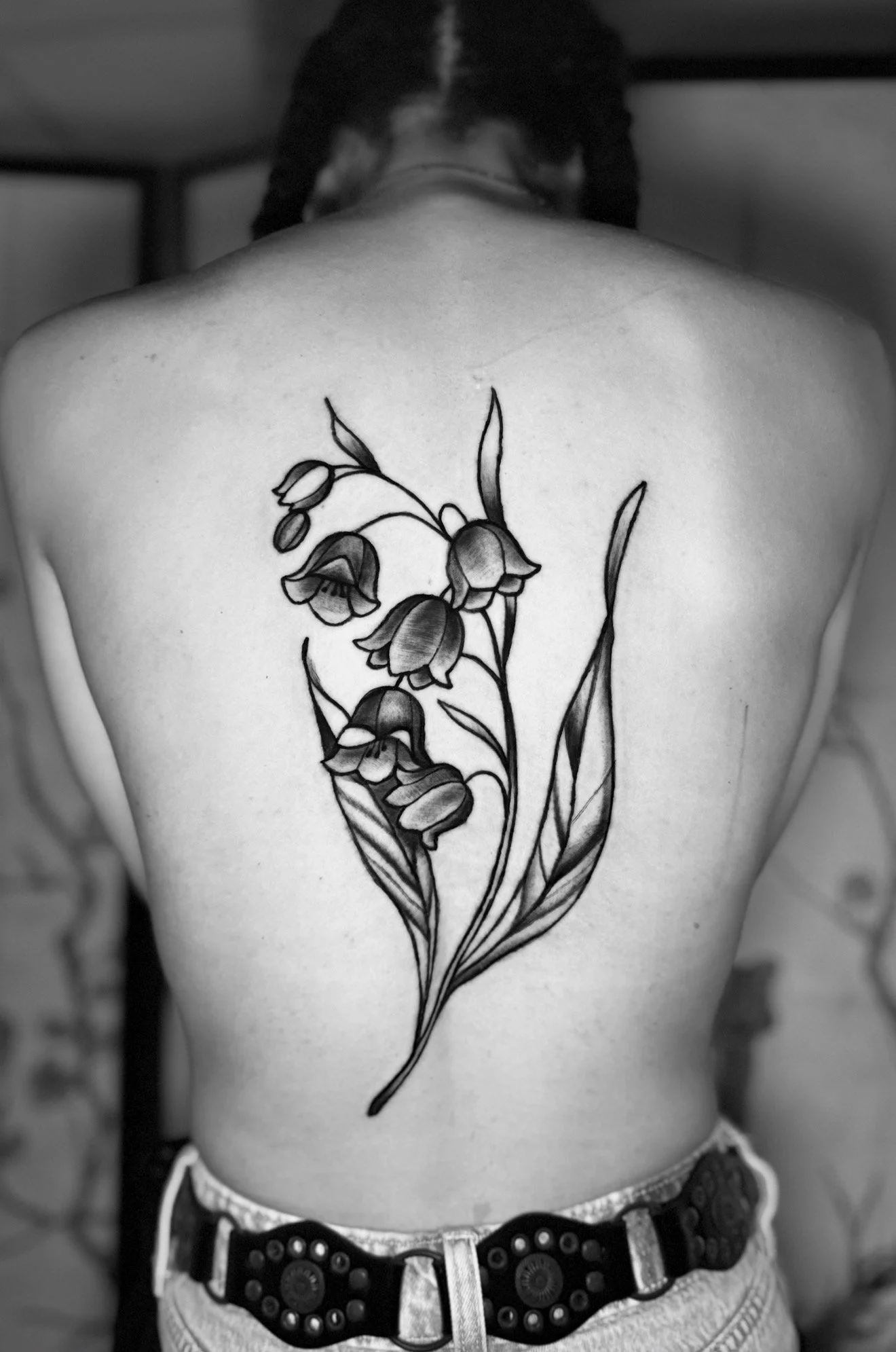 Black and white photo of a person's back showing a large floral tattoo with multiple bell-shaped flowers and long leaves.