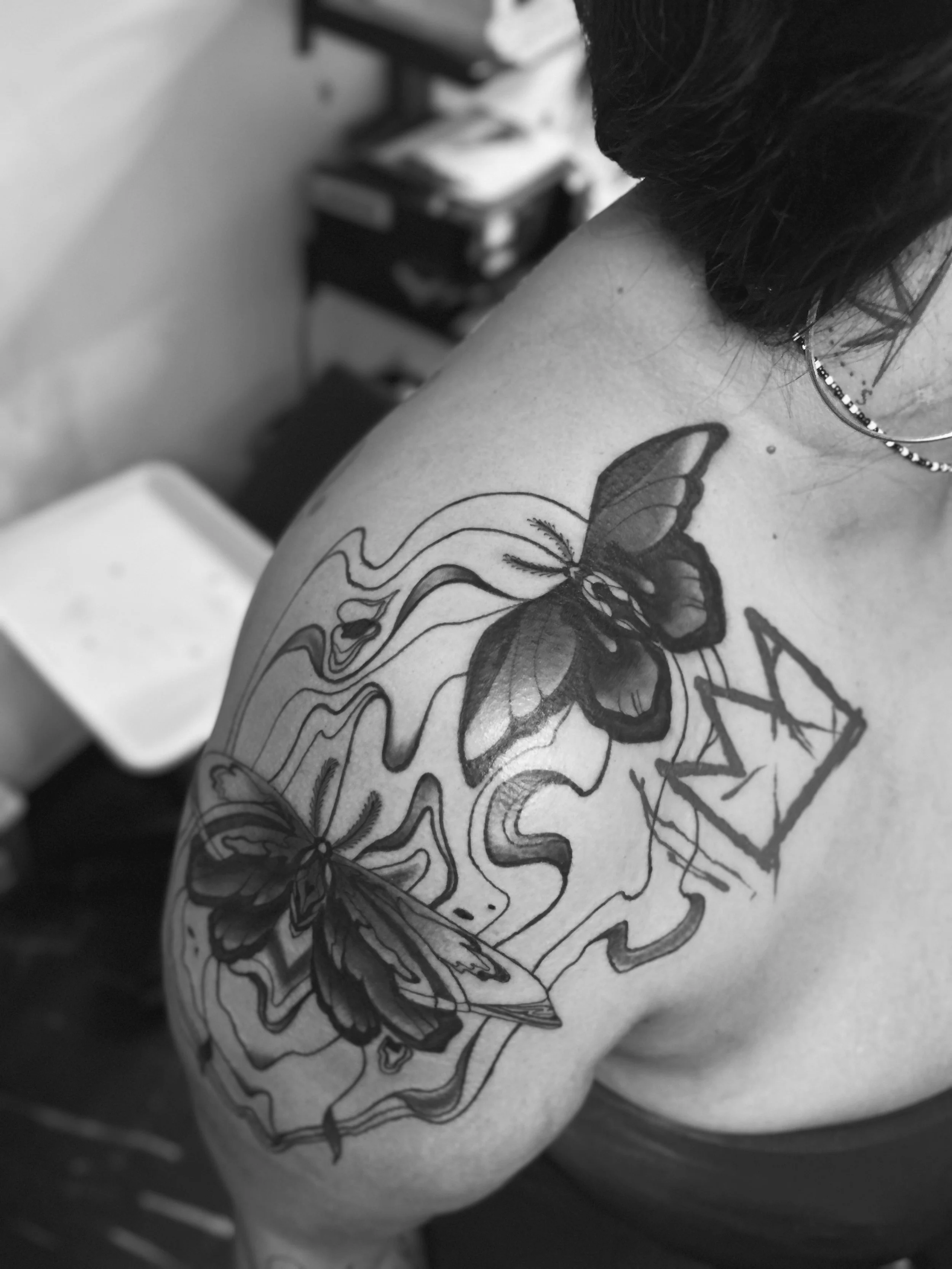 Black and gray tattoo of two butterflies, one above the other, with flowing lines and abstract design on a person's shoulder.