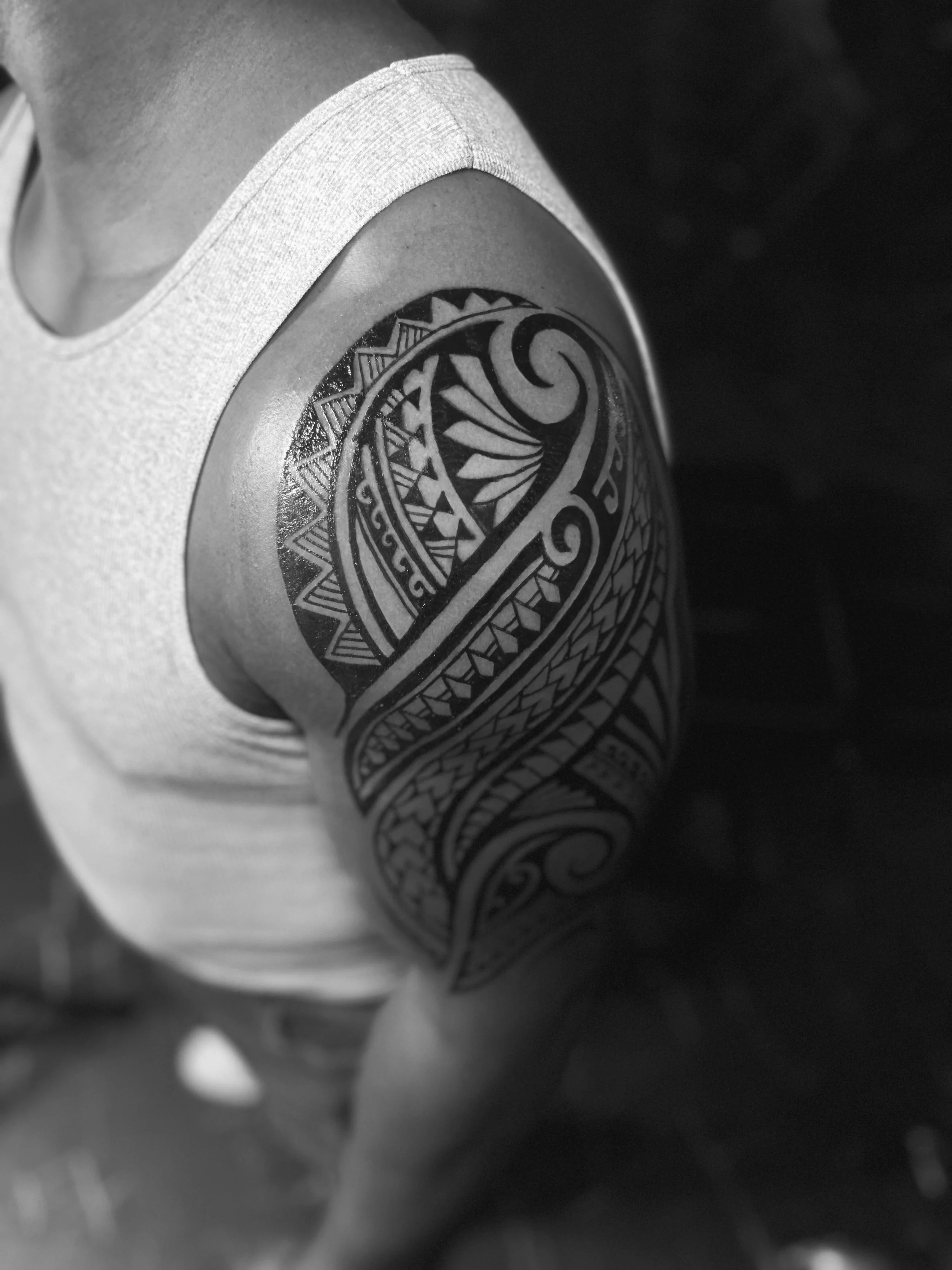 Black and white photo of a person wearing a sleeveless shirt with an intricate tribal tattoo on their upper arm.