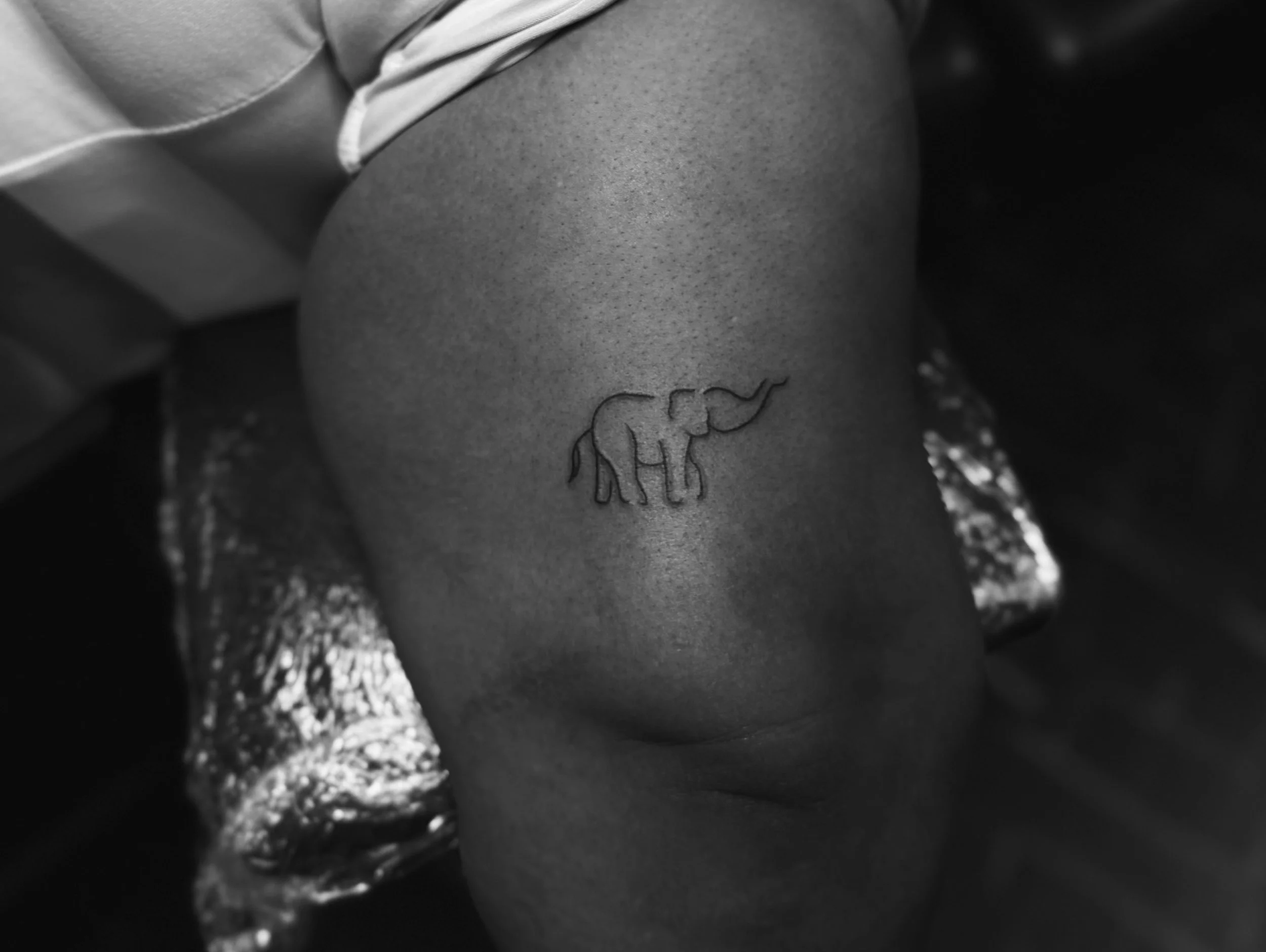 Close-up of a person's thigh with a tattoo of an elephant on it in a black and white photo.