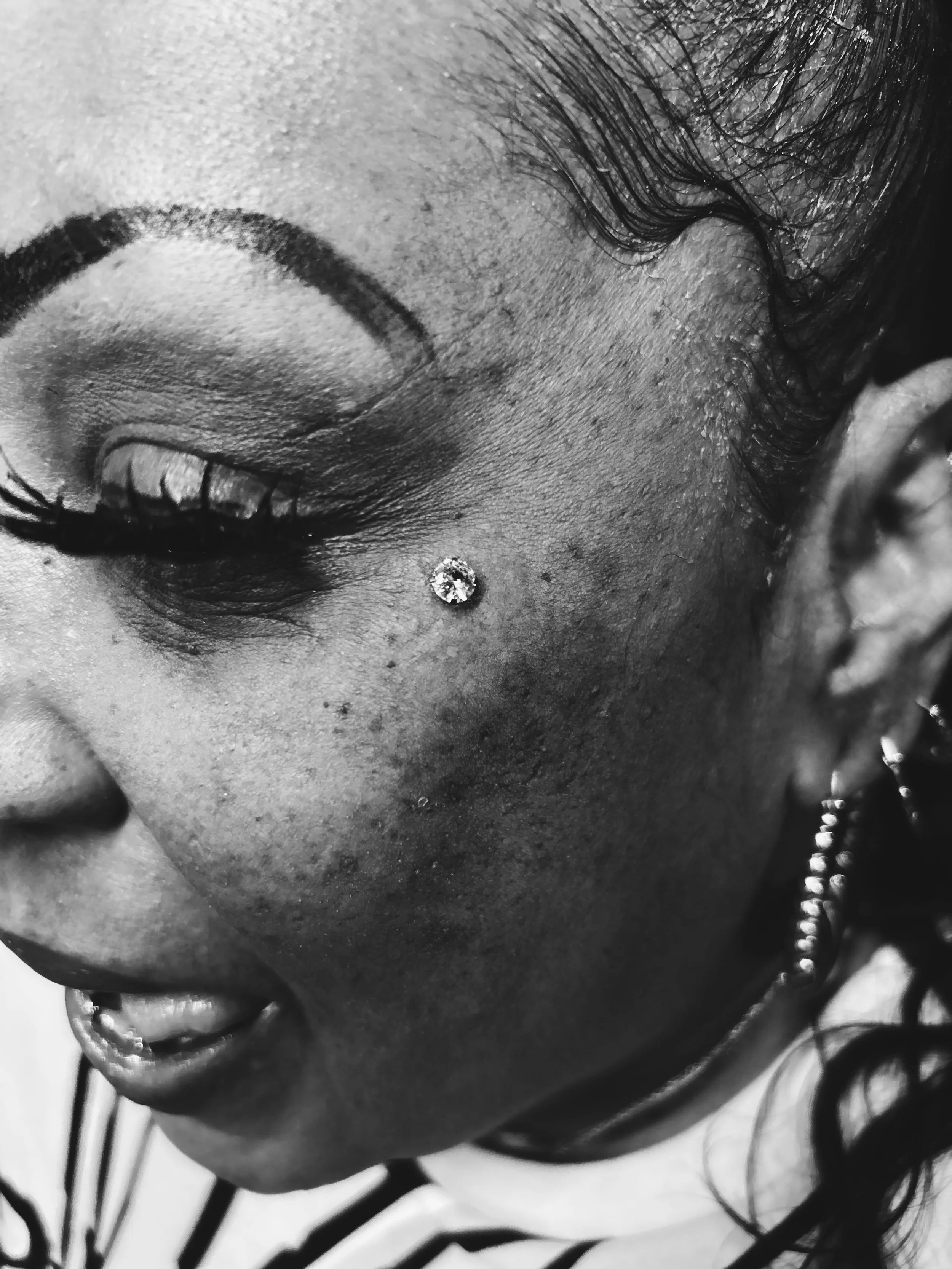 Close-up of a woman's face with eye makeup and earrings, wearing a striped top.