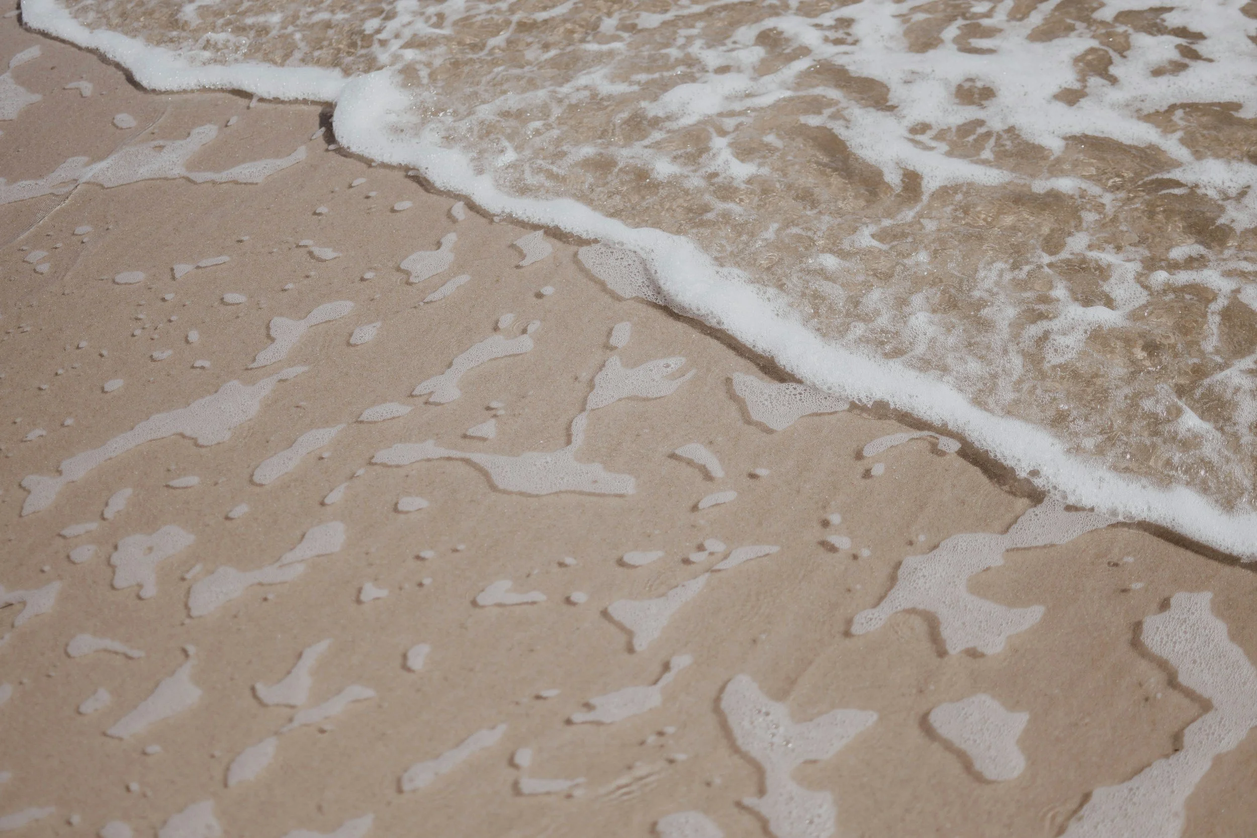 Close-up of gentle waves washing onto a sandy beach.