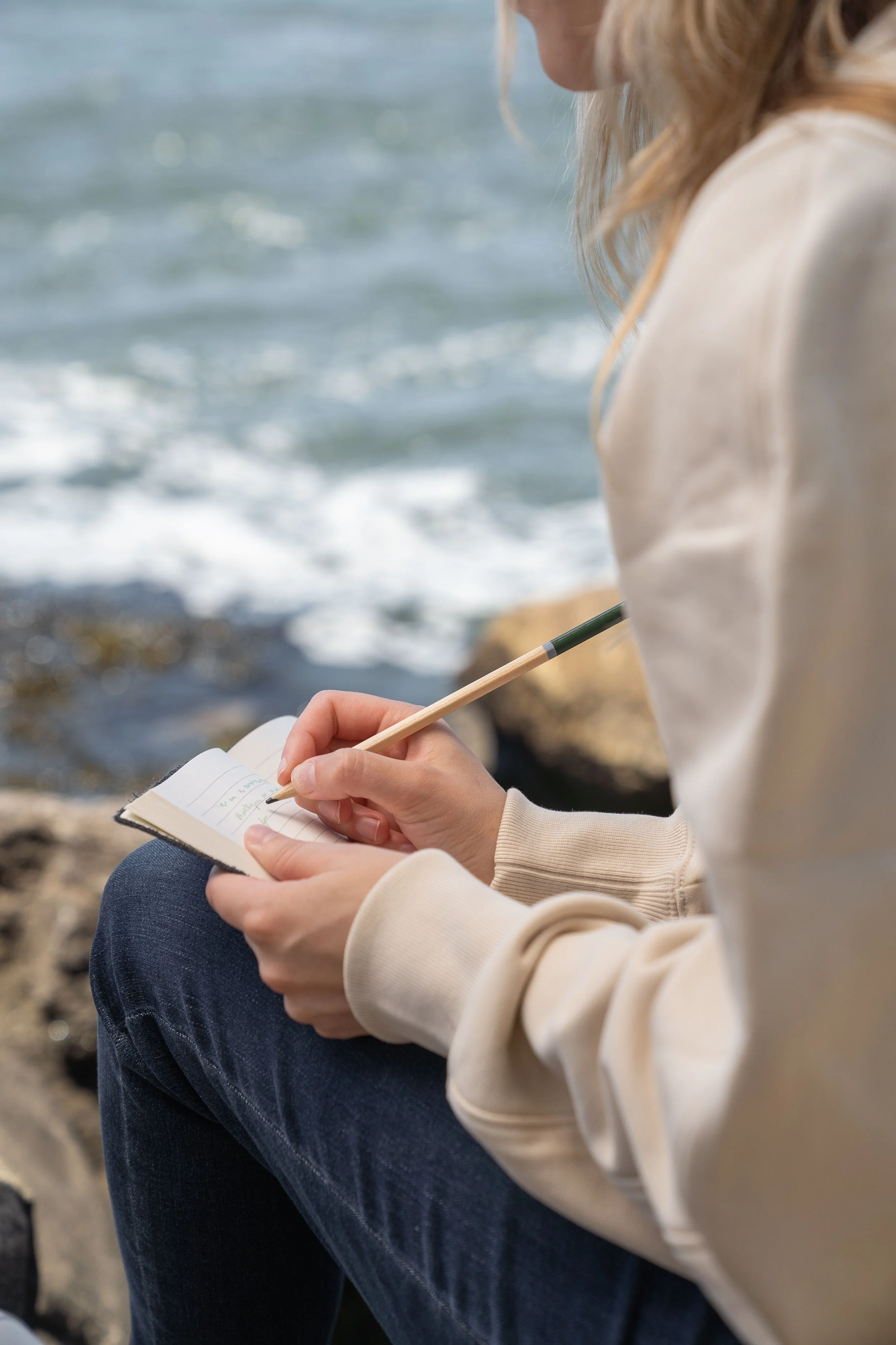 Woman journaling while sitting near the ocean