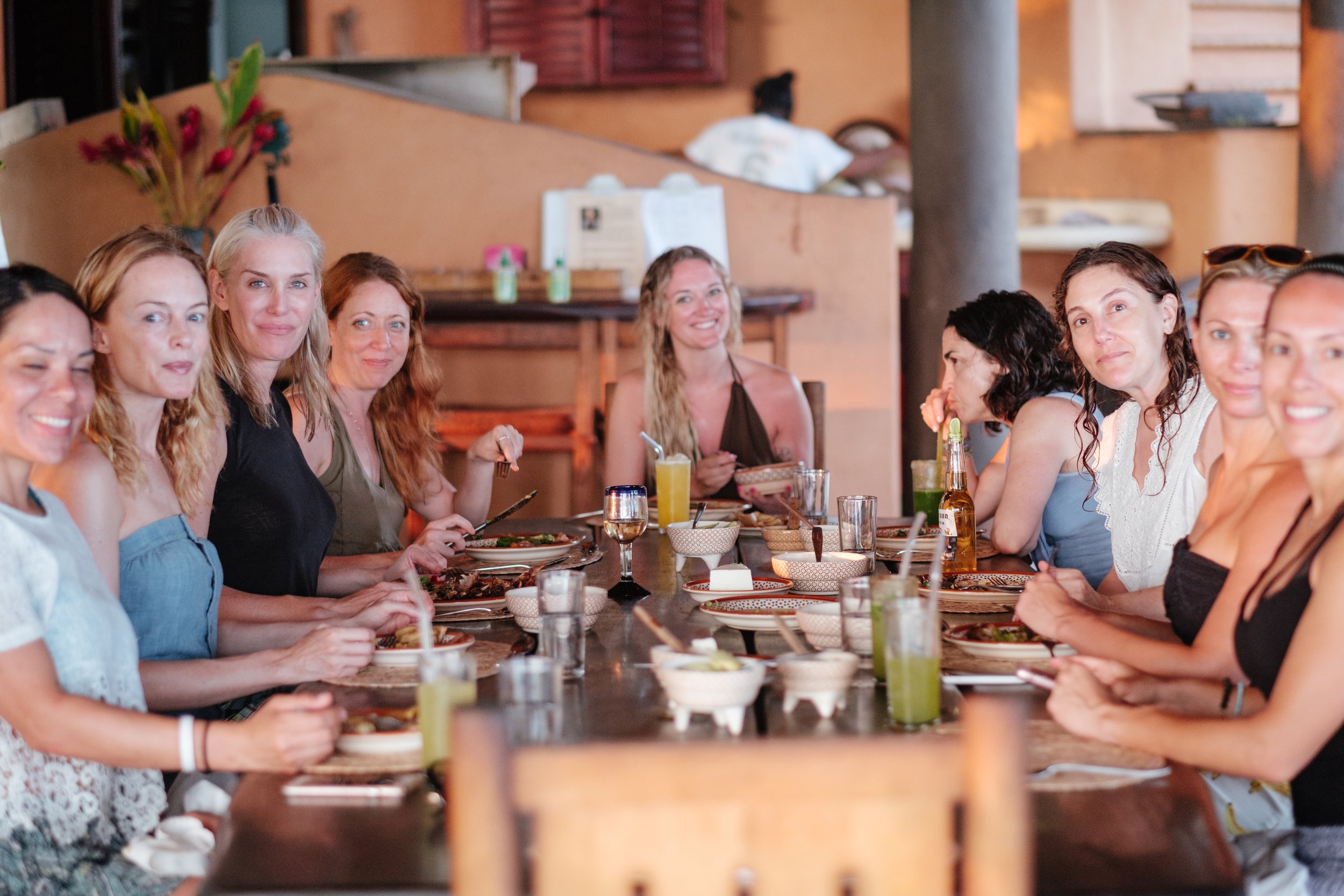 Group of women sitting at a long dining table in a restaurant, smiling and enjoying their meal.