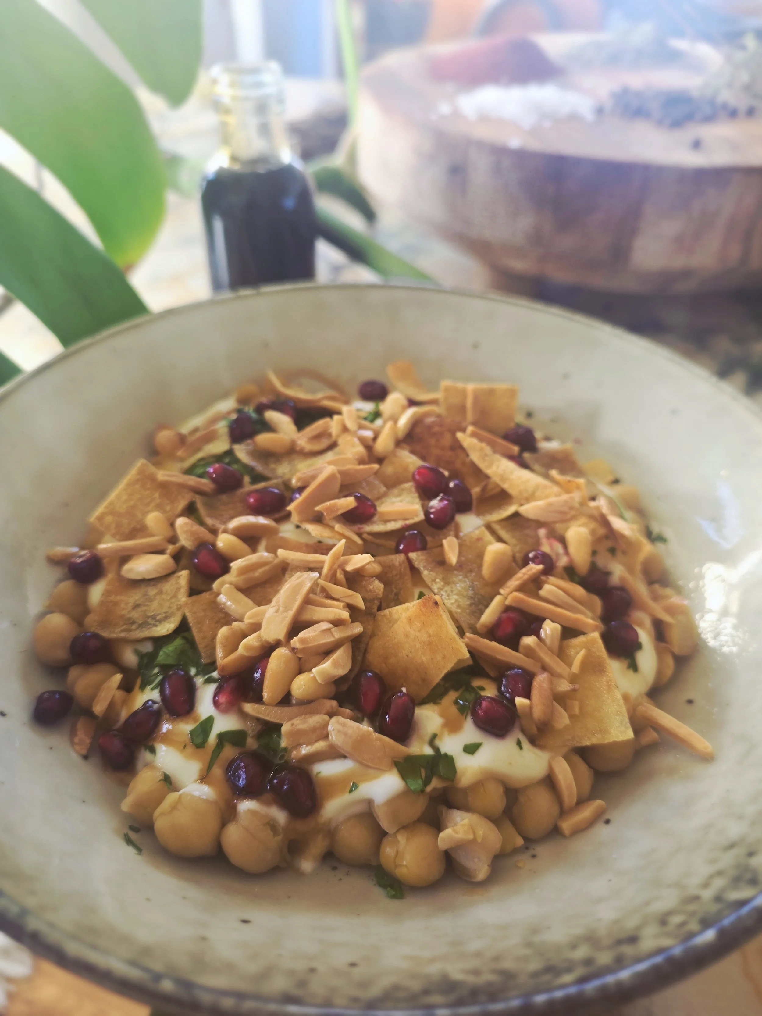A bowl if chickpeas and yoghurt topped with pomegranate seeds, toasted pine nuts, chopped parsley, and crispy pita chips.