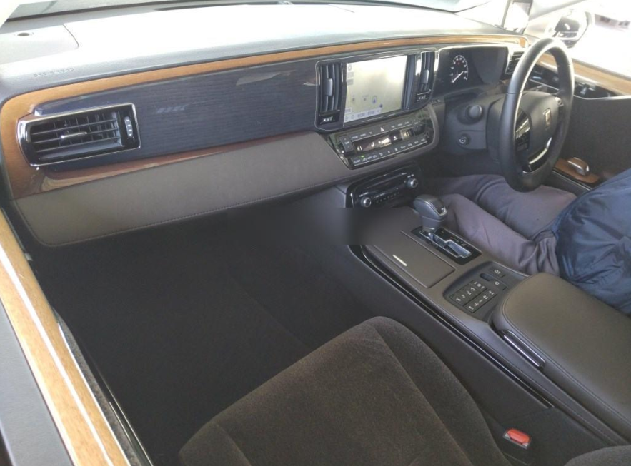 Interior of a car featuring a wood and leather dashboard, touchscreen display, gear shift, and steering wheel.