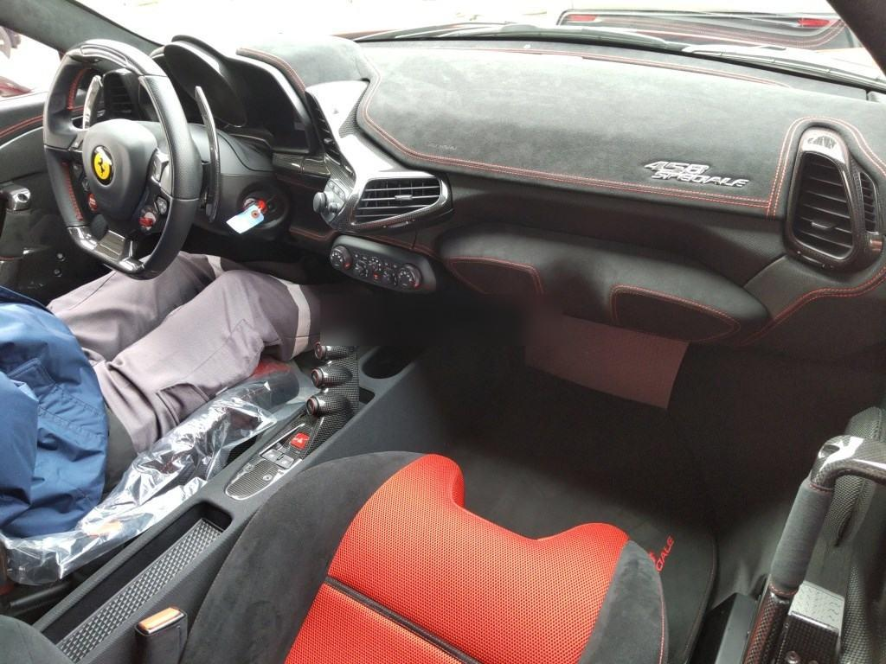 Interior of a sports car showing a steering wheel with a Ferrari logo, a red racing seat, and various control buttons and vents on the dashboard.