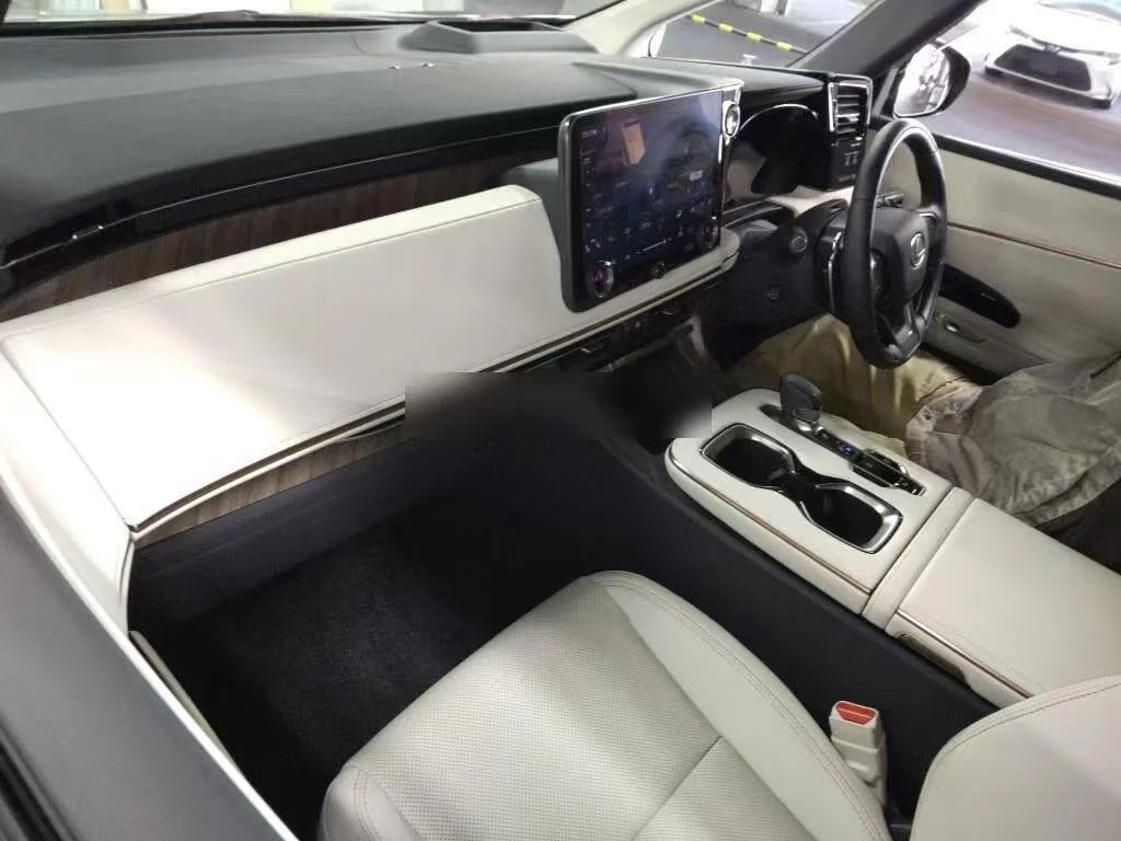Inside view of a modern vehicle's dashboard and front seats, featuring a large touchscreen display, steering wheel, gear shift, and center console with cup holders.
