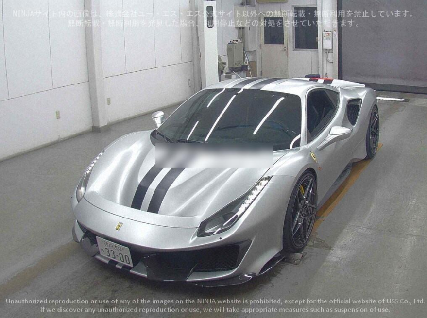 A silver Ferrari sports car with black racing stripes on the hood, parked inside a garage or parking area.
