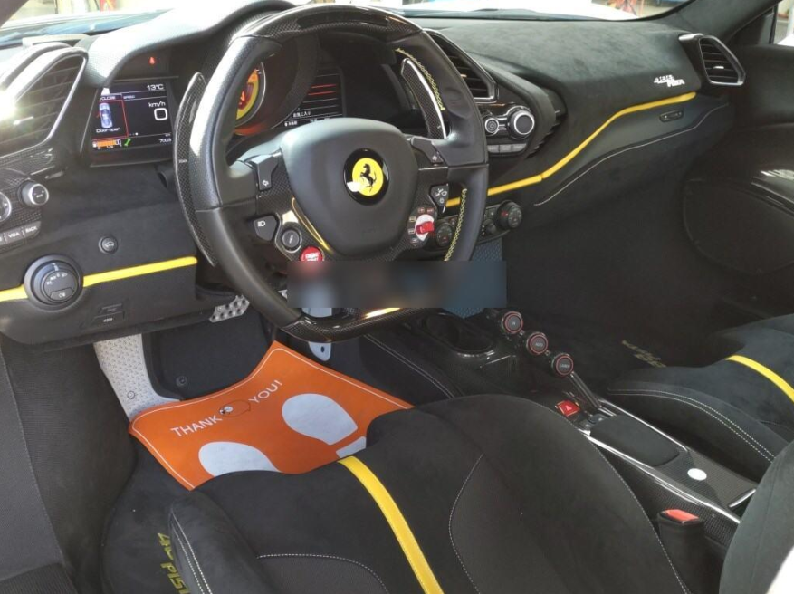 Interior of a Ferrari race car with a yellow and black steering wheel, digital dashboard, and racing seats with yellow accents.