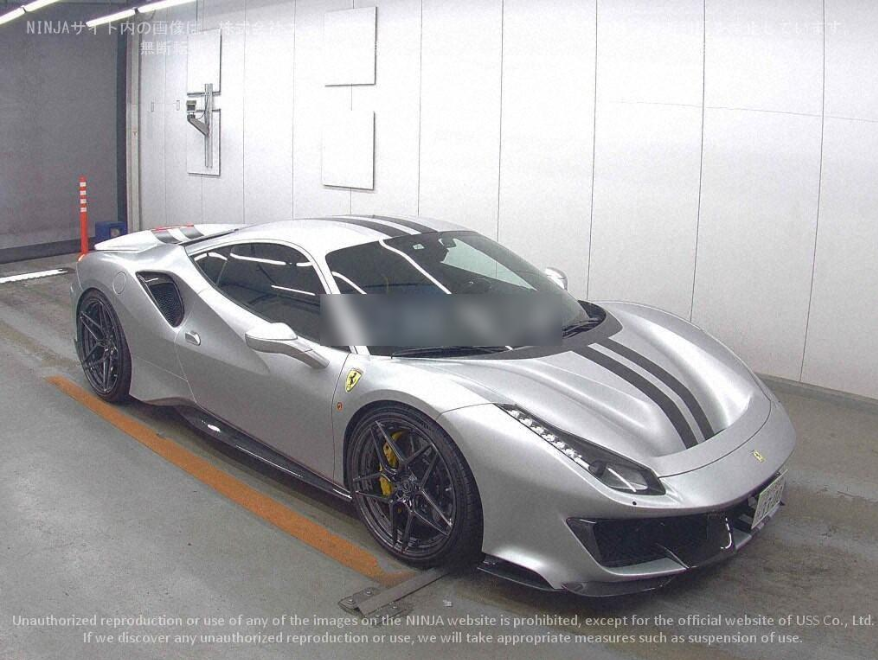 A silver Ferrari sports car with black racing stripes parked in an indoor garage.