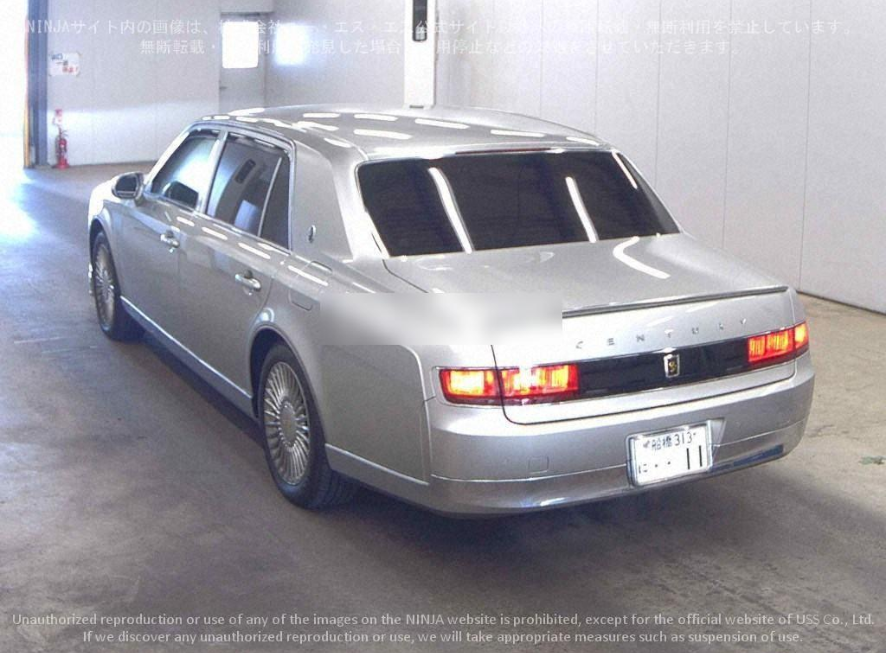 Silver sedan car in an indoor garage with Japanese license plates, reflecting ceiling lights, with a rear view showing taillights and trunk.