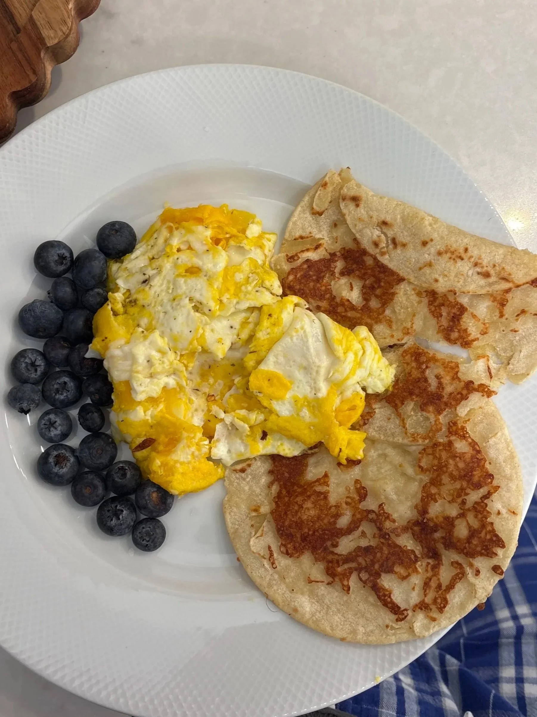 Plate of breakfast featuring scrambled eggs, blueberries, and two tortillas.