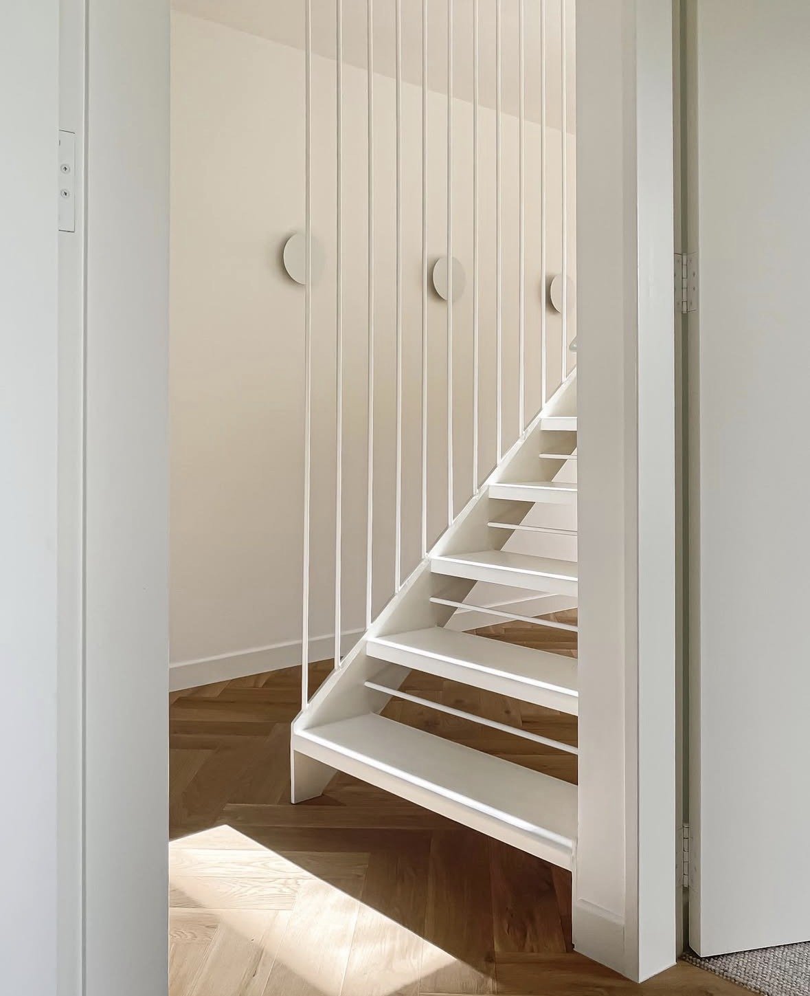 White staircase with open risers against a white wall with vertical paneling.
