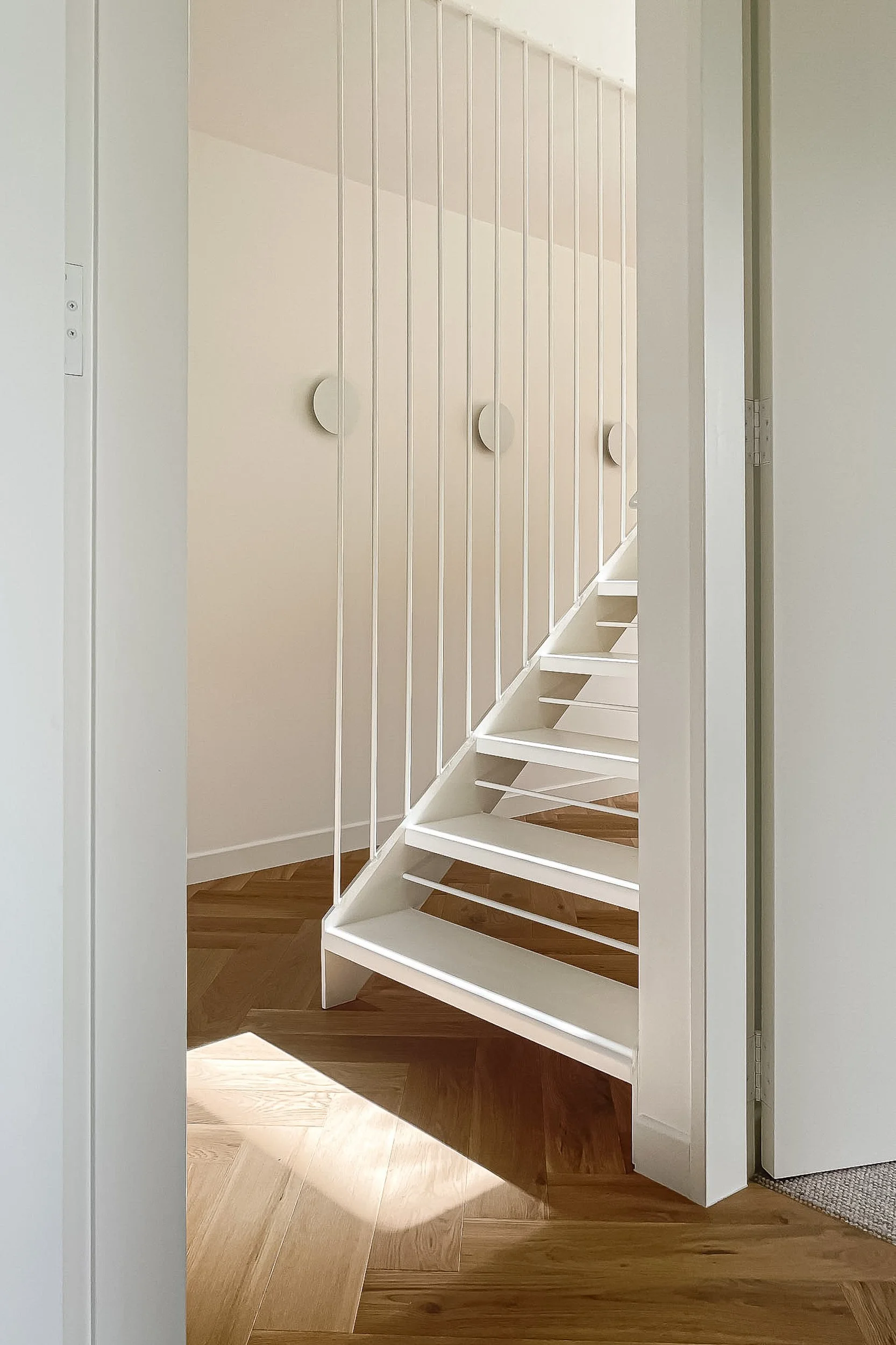 A white spiral staircase with open risers, located in a modern interior space with light wood flooring and white walls.