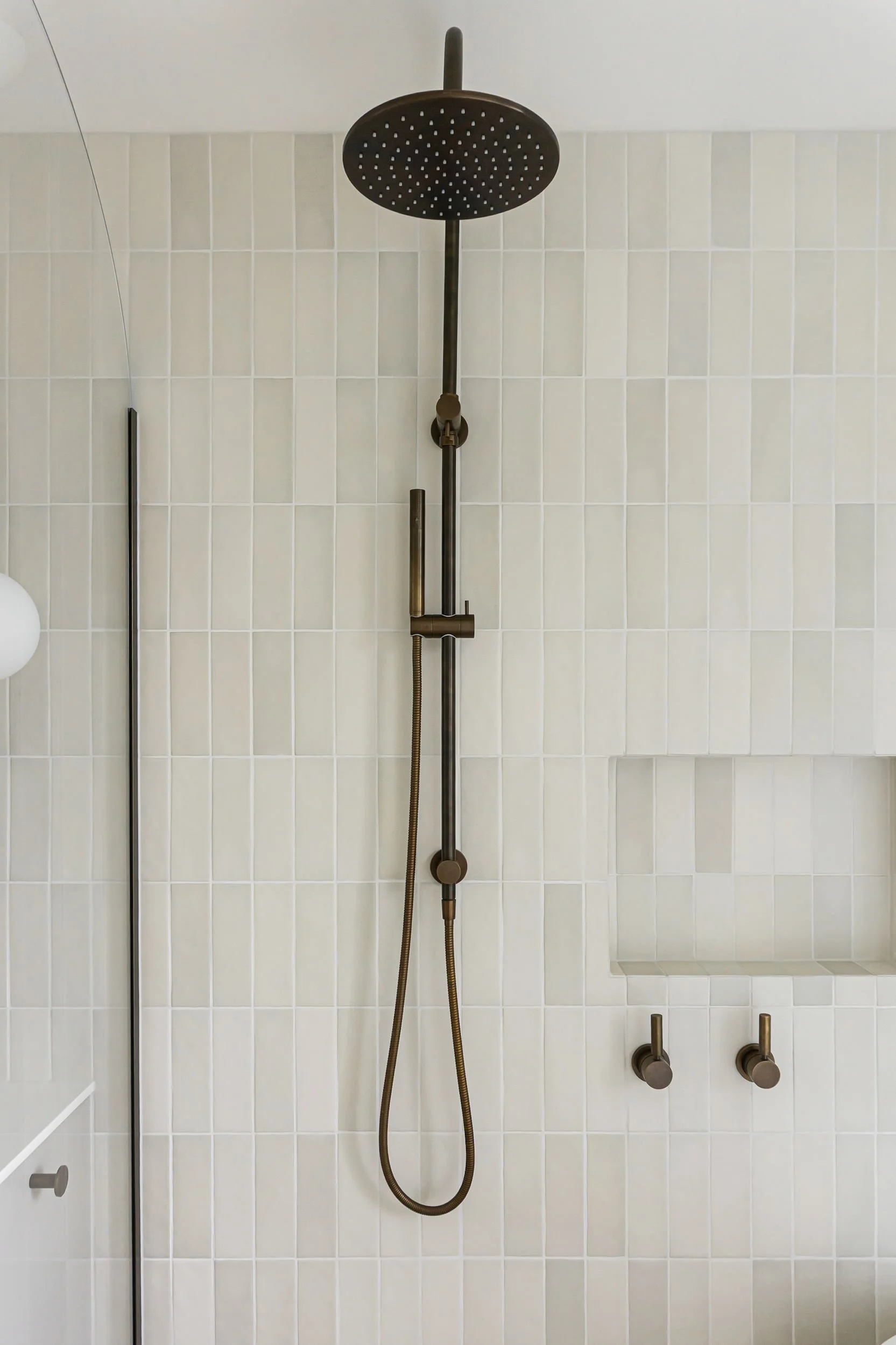Modern shower area with round overhead shower head, a hand-held shower, and controls on a tiled wall.