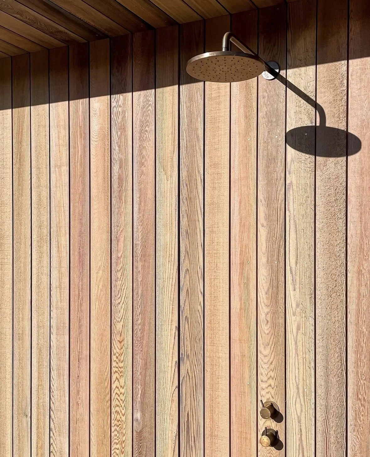 Wood-paneled outdoor shower with a rainfall showerhead and two knobs for water control.