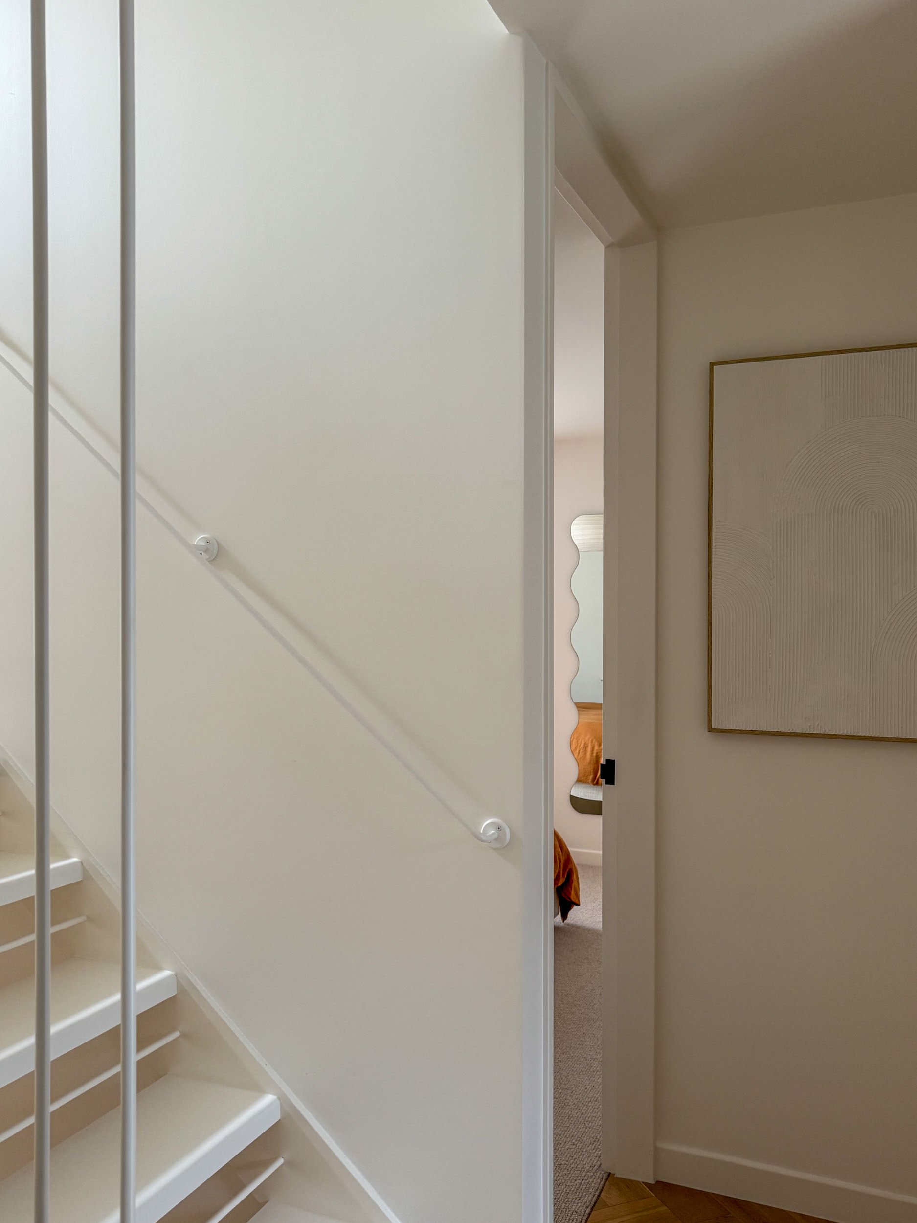 View of a staircase with white walls, a handrail, and a partially open door leading to a room with a bed and a piece of wall art.