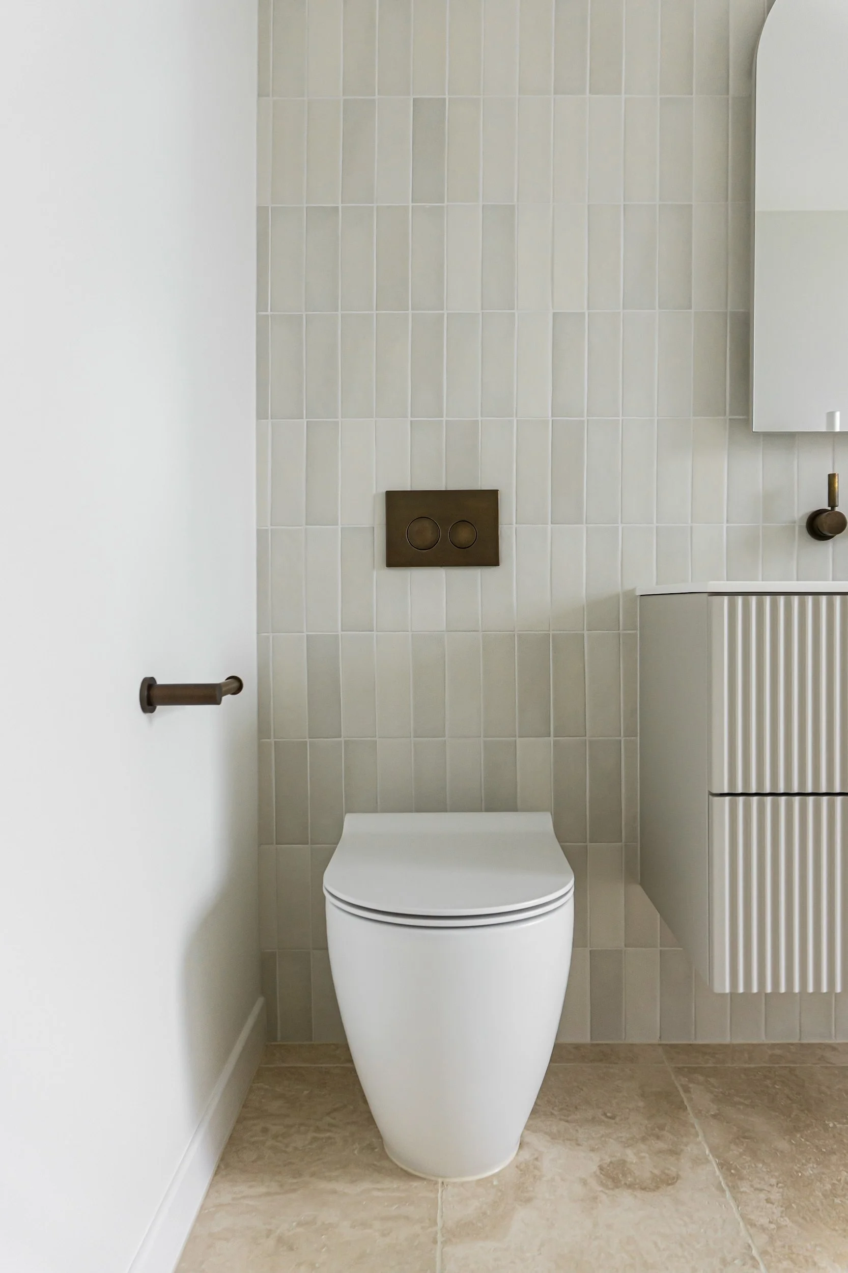 A modern bathroom with a white toilet, beige tiled wall, and a brown dual-flush button on the wall.