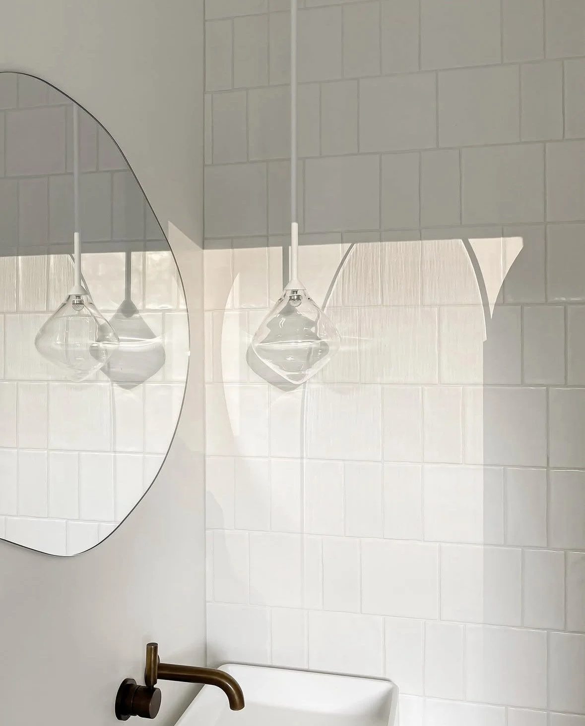 A bathroom with a wall mirror reflecting a hanging glass light fixture, tiled walls, a white sink, and a bronze faucet.