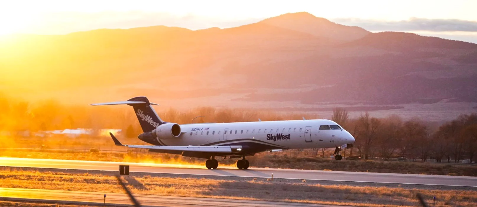 A SkyWest airplane landing on a runway at sunset with mountains in the background.