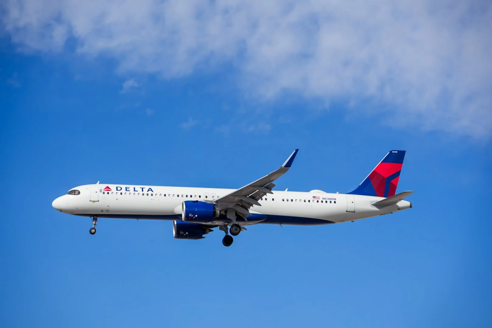 A Delta Airlines commercial airplane flying through a partly cloudy sky.