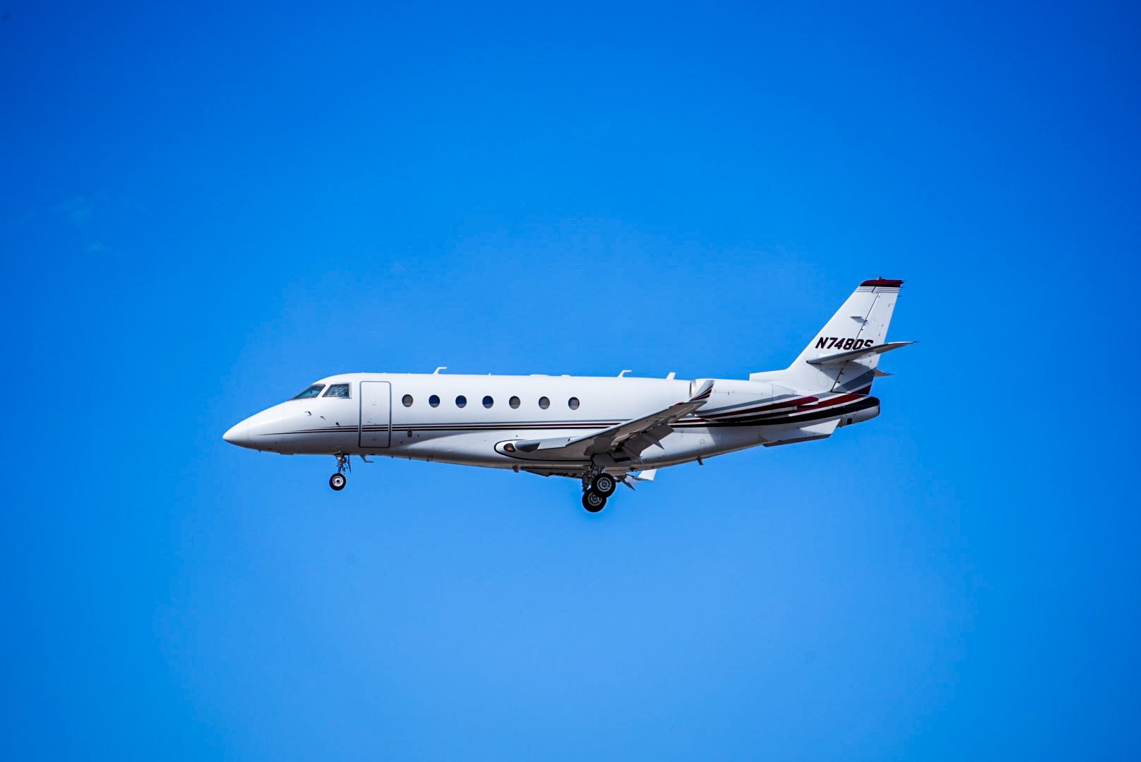 A white private jet airplane flying against a bright blue sky.